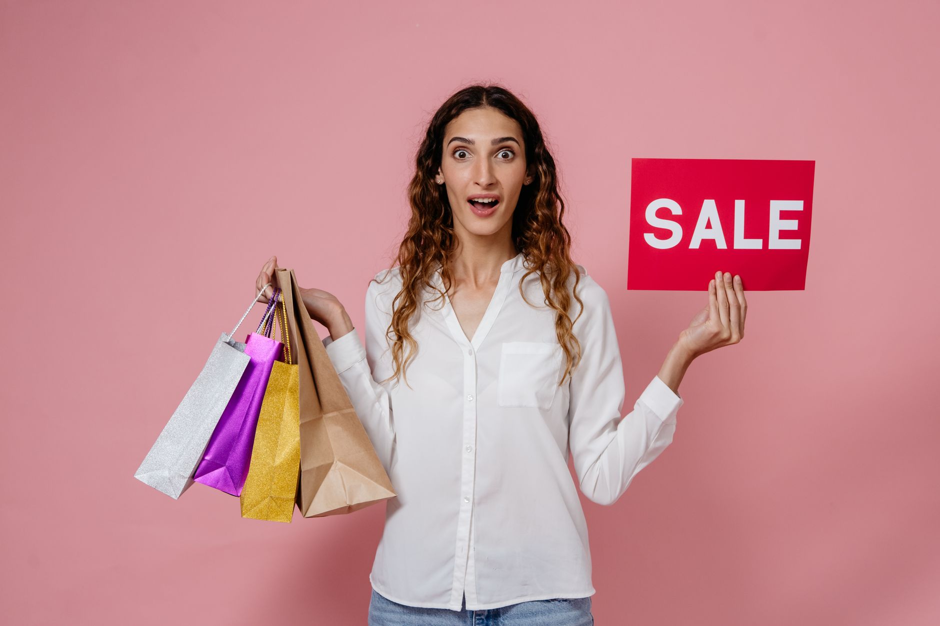 Woman holding shopping bags and sale sign, expressing surprise and excitement.