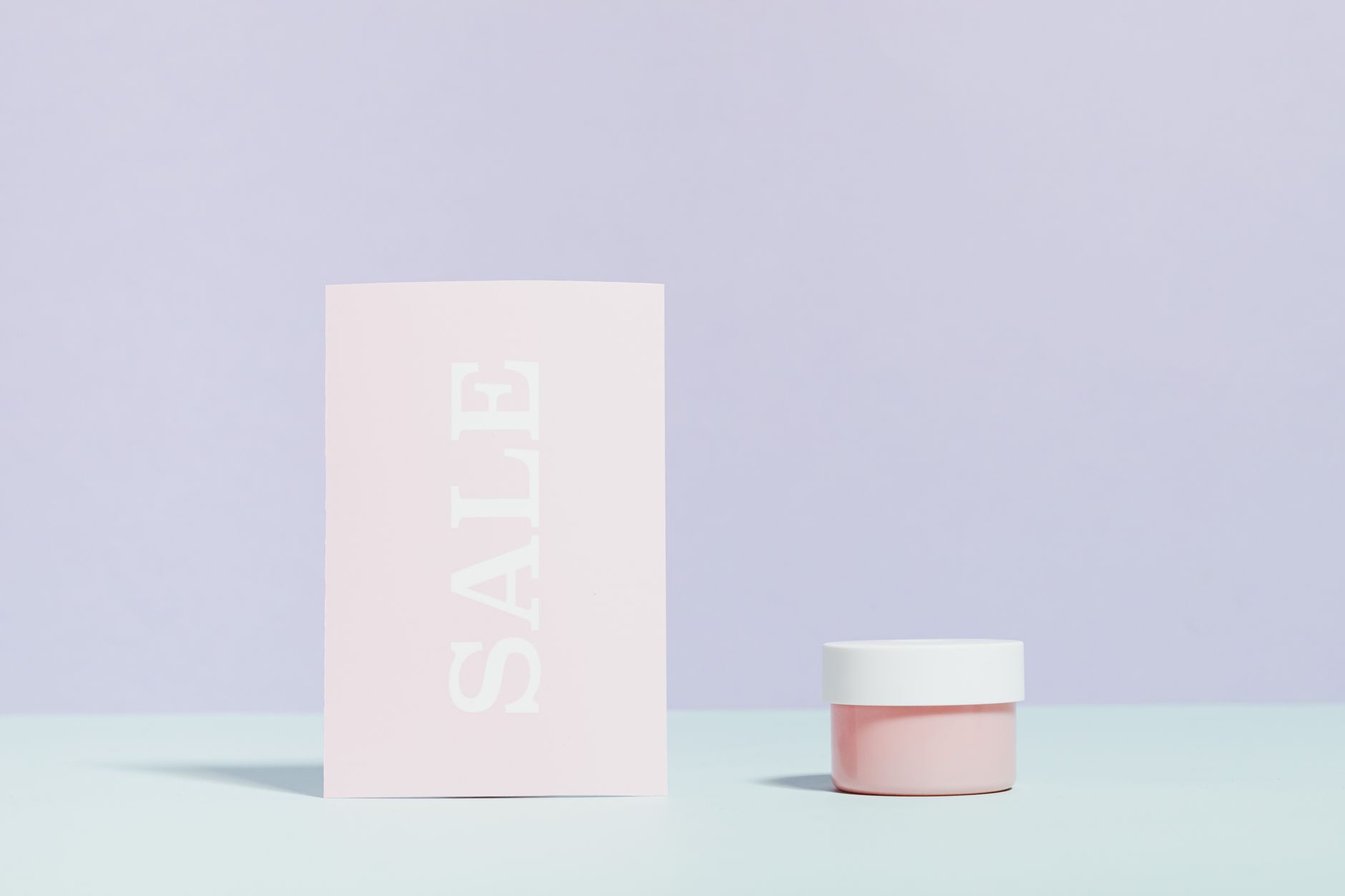 Elegant still life of a sale card and cream jar on pastel background.