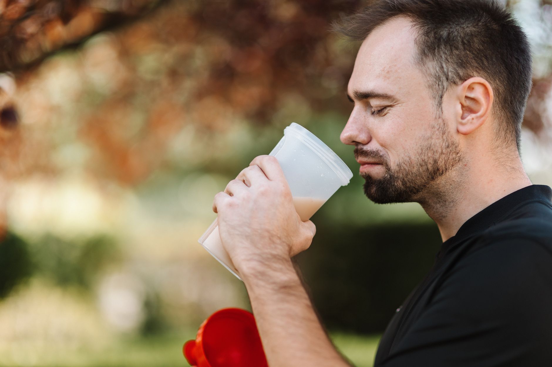 Adult man savoring a protein shake in a peaceful outdoor setting during the day.