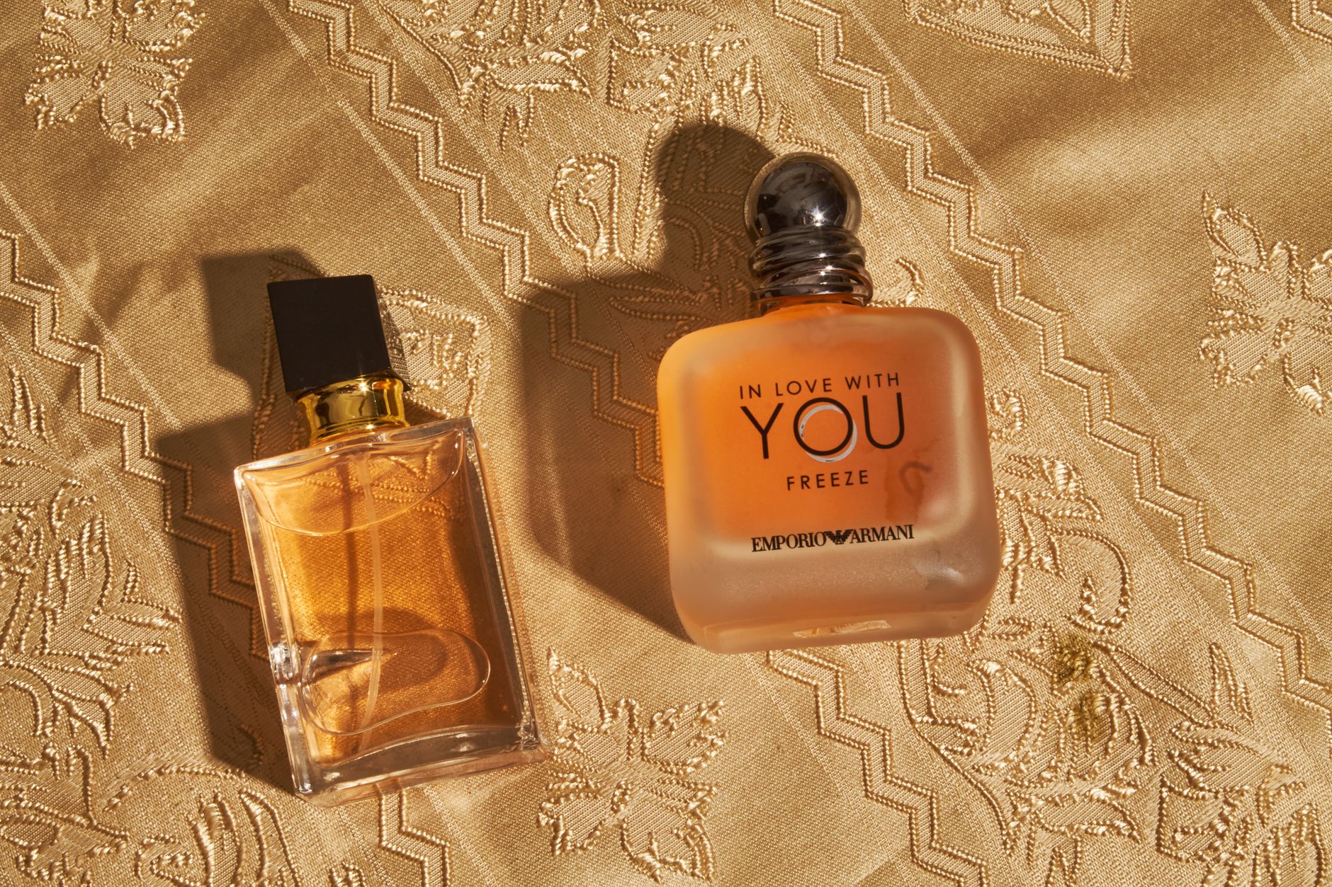 Two elegant perfume bottles resting on intricately patterned golden fabric create a luxurious aesthetic.
