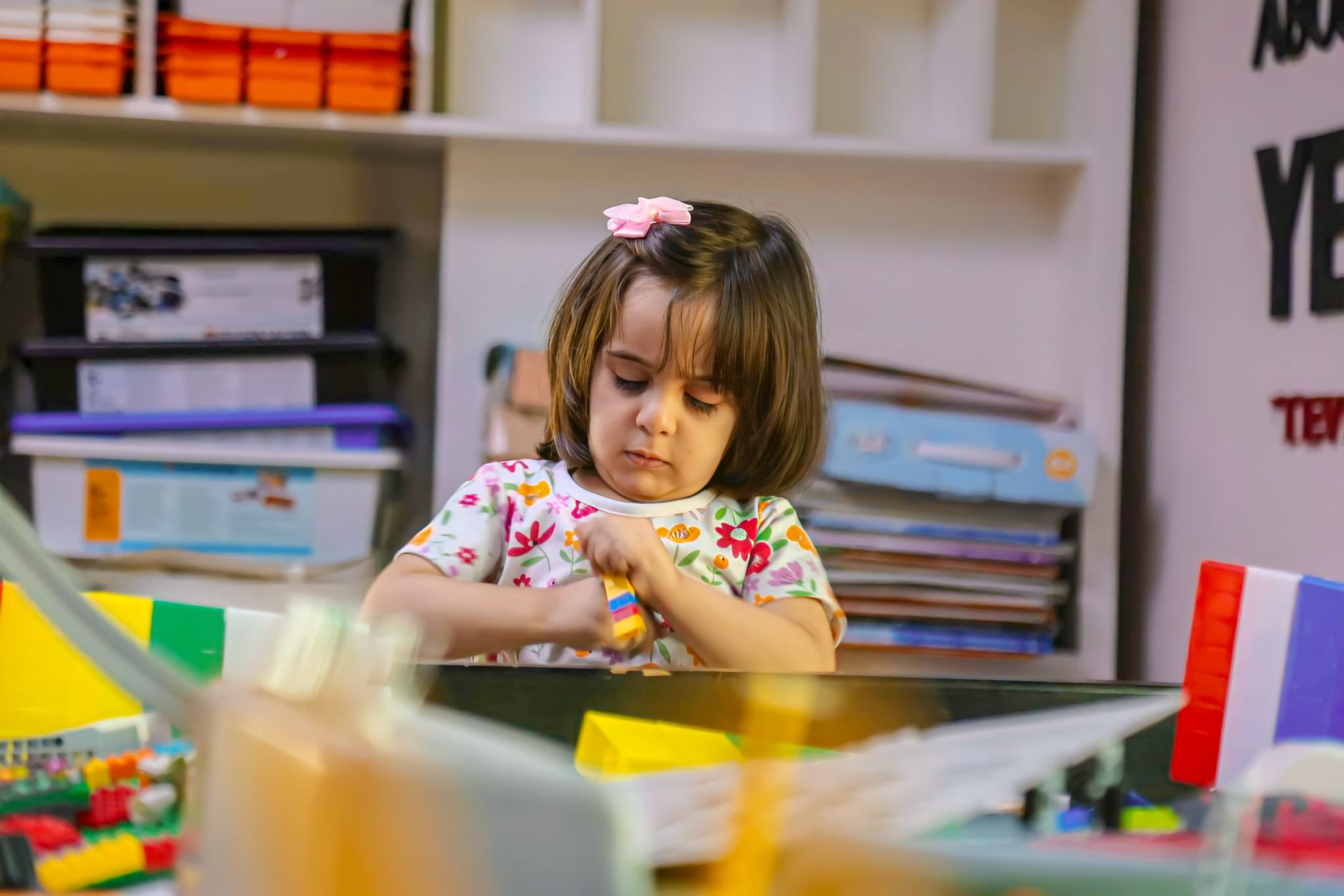 A young girl with a hair clip plays with colorful toys indoors, focused and engaged.