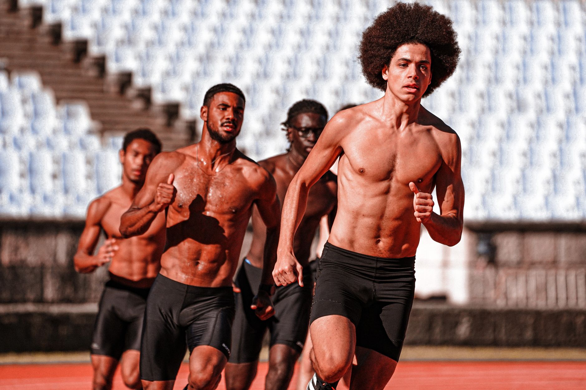 A group of diverse male athletes running on an outdoor track, showcasing strength and endurance.