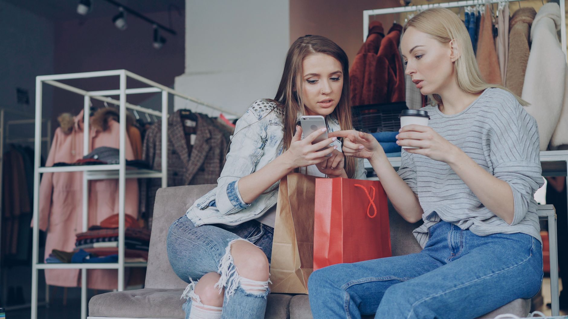 Two women in a clothing store sharing a smartphone moment while shopping.