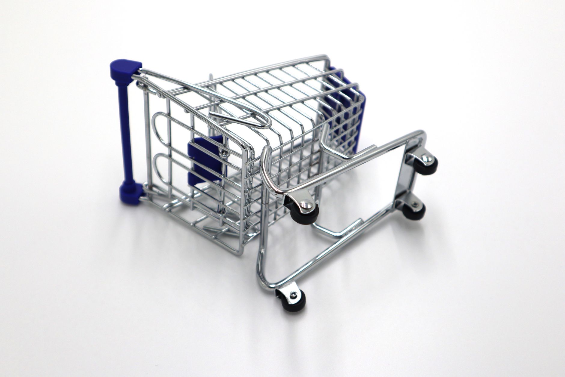 A flipped miniature shopping cart on a white surface symbolizes retail challenges and economic concepts.