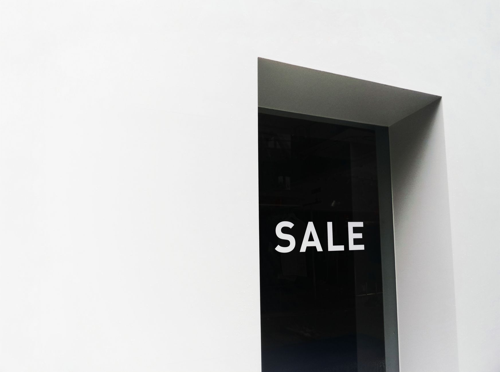 A minimalist black and white image of a sale sign on a store window with ample negative space.