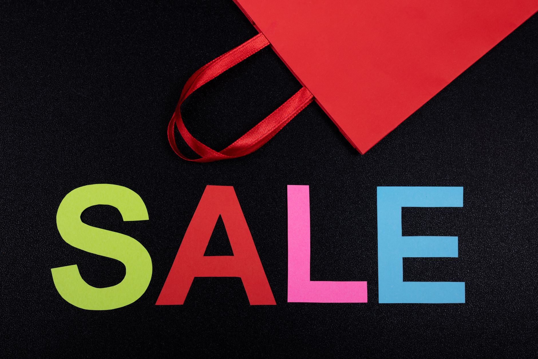 Vibrant text 'SALE' next to a red paper bag on a black background.
