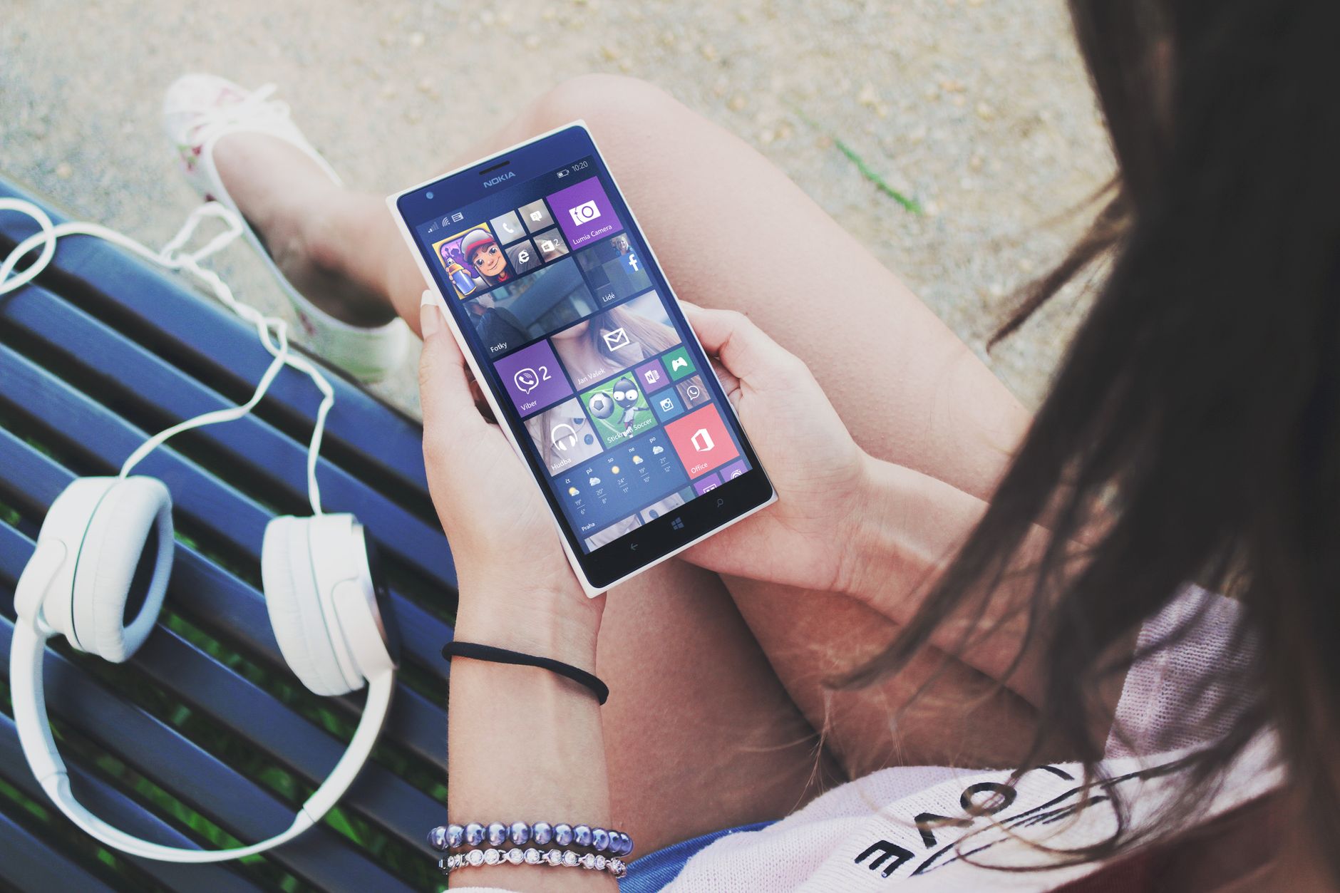 Close-up of a woman using a Windows smartphone with headphones outdoors.