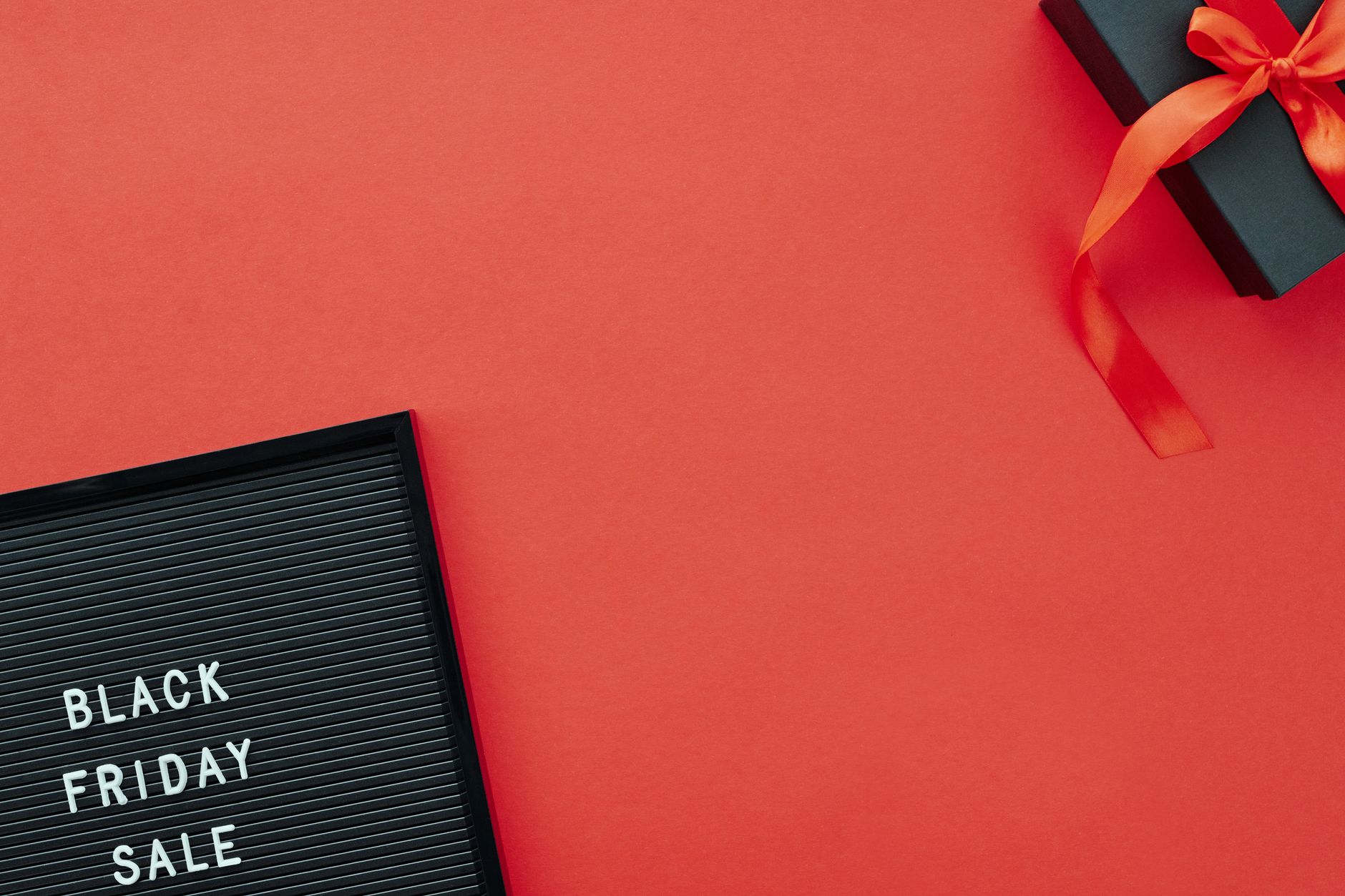 Top view of a Black Friday sale sign and gift box on a vibrant red background.
