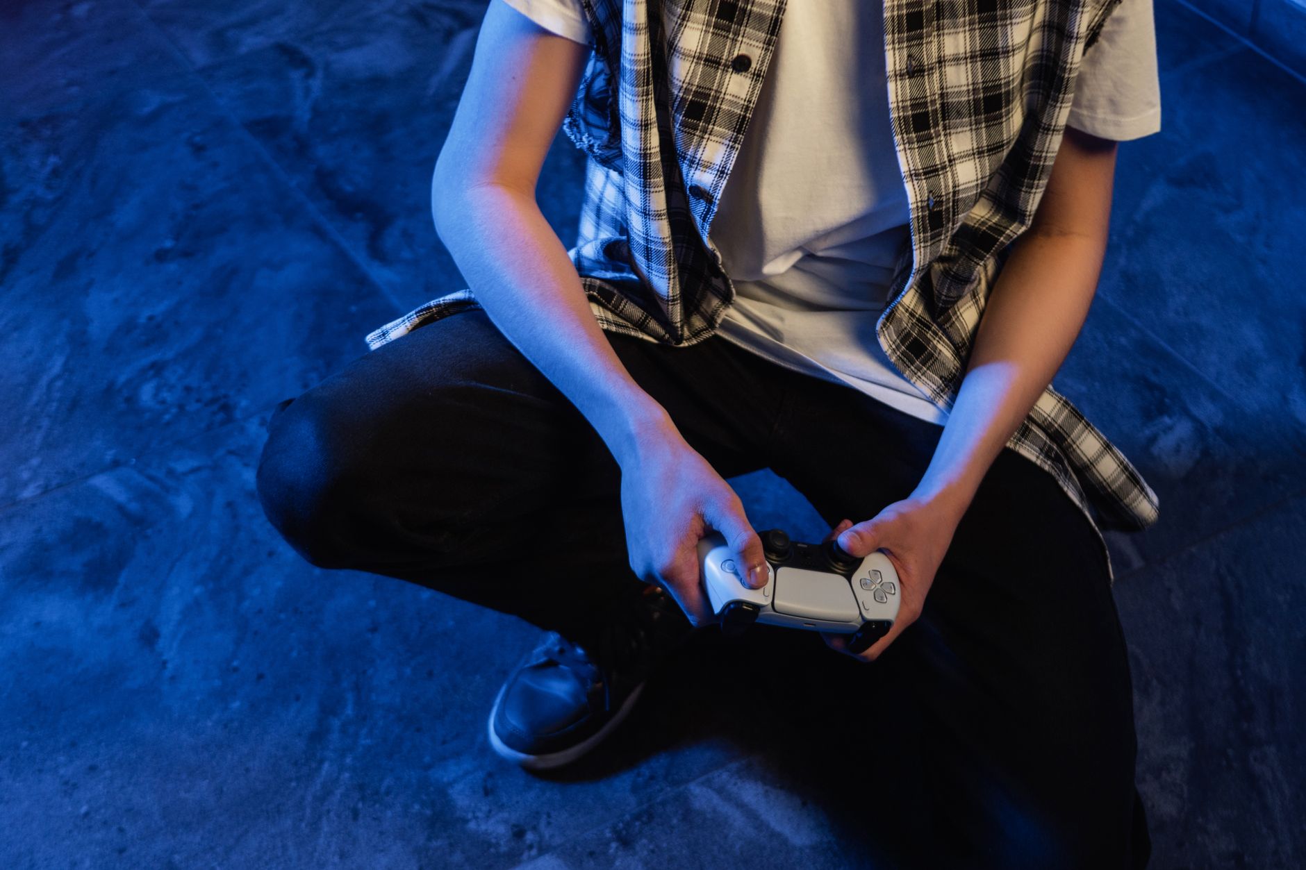 A young person intensely focused on gaming with a joystick in a blue-lit room.