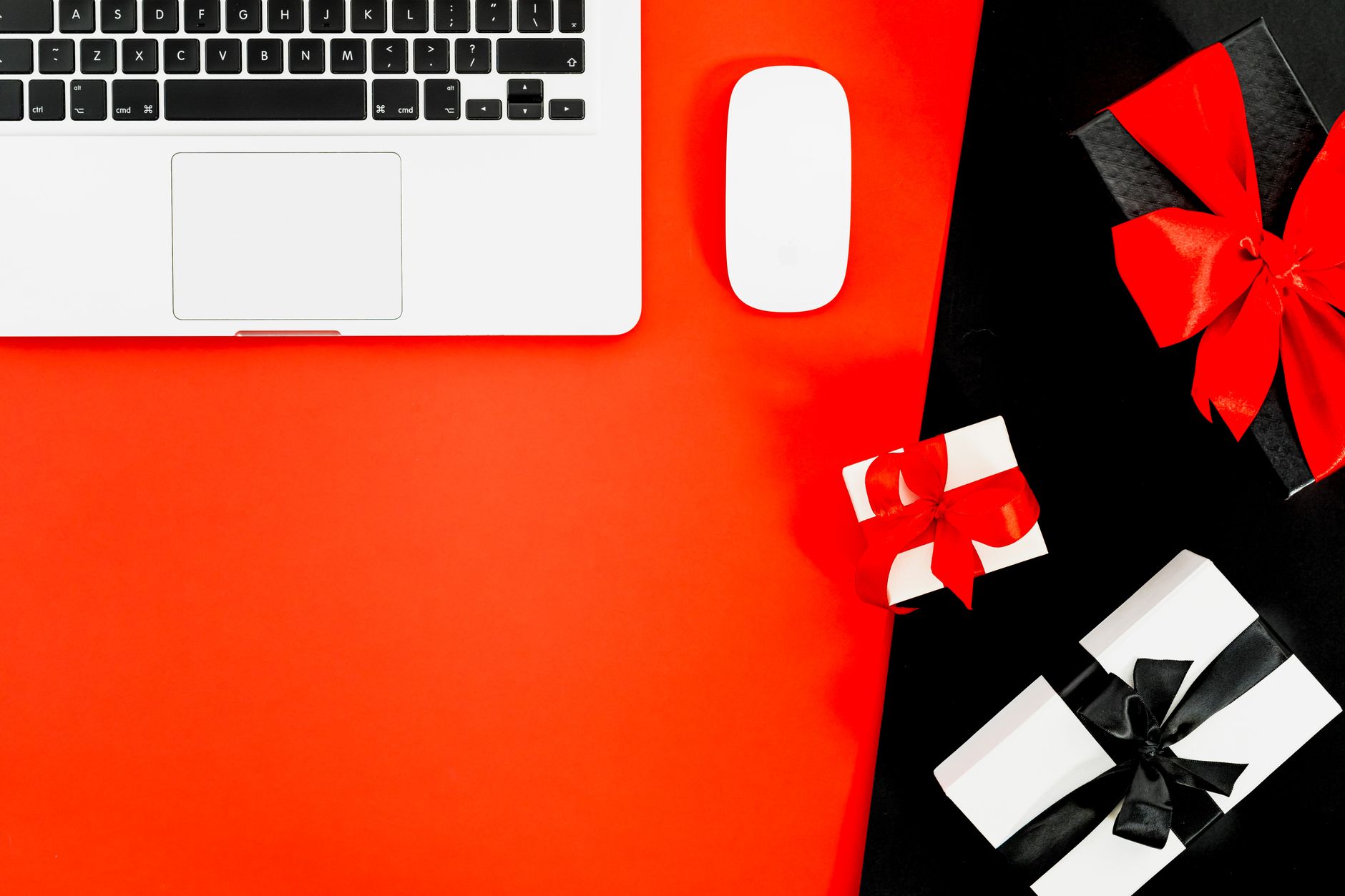 Flat lay of laptop with gift boxes on red background, perfect for holiday shopping themes.