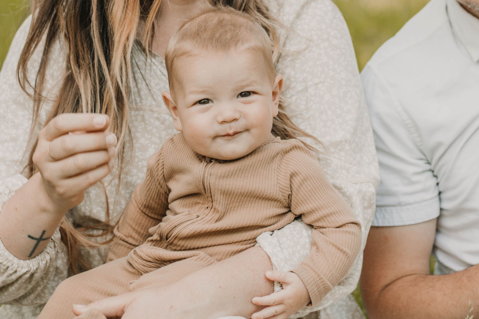 A cozy and candid family moment with a baby embraced by parents in a serene outdoor setting.