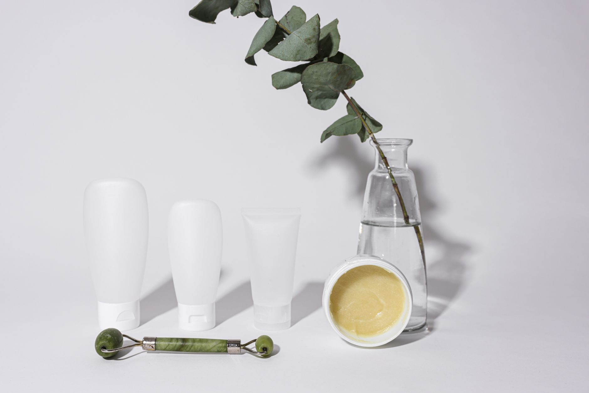 Elegant studio shot of skincare products with jade roller and vase, ideal for beauty and wellness themes.