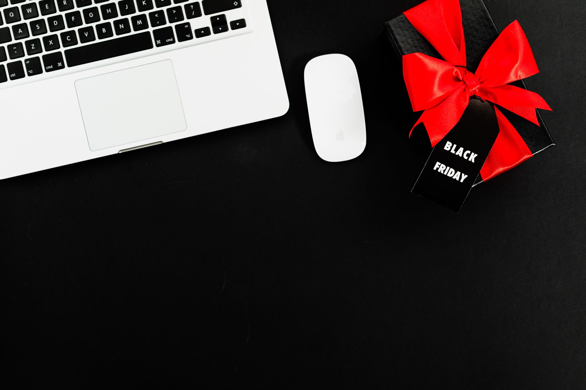 Flat lay of a laptop and Black Friday gift box with red bow, perfect for online shopping themes.