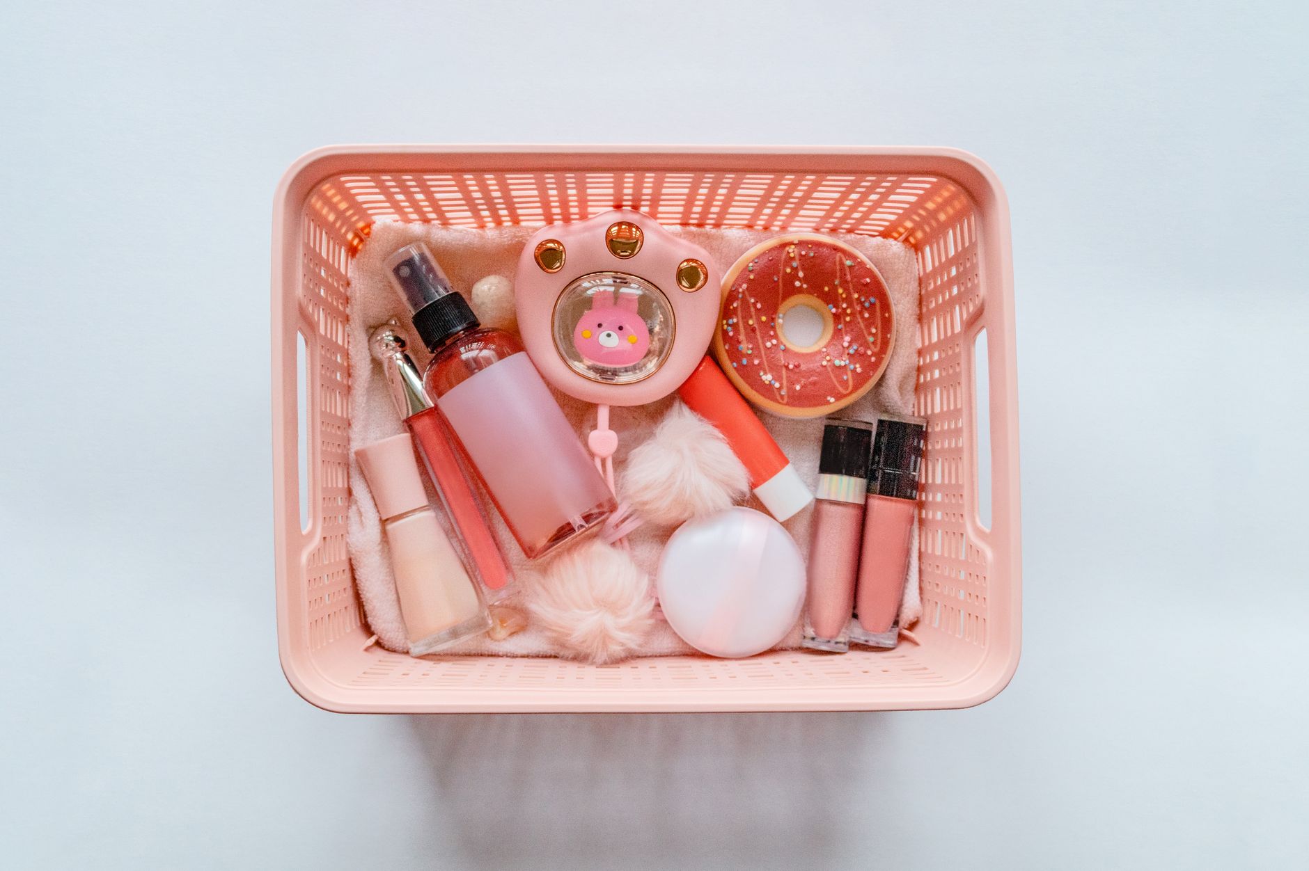 Flatlay of pastel pink cosmetics organized in a basket, ideal for beauty and self-care themes.