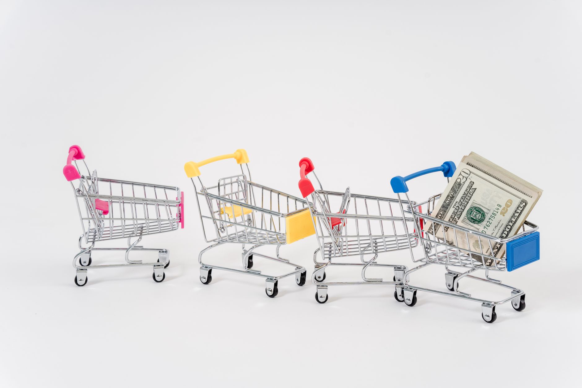 Miniature shopping carts in bright colors with dollar bills imply financial shopping themes.