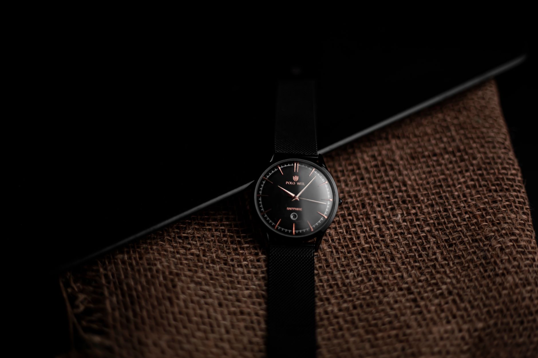 Stylish black wristwatch displayed on burlap with a dark elegant background.