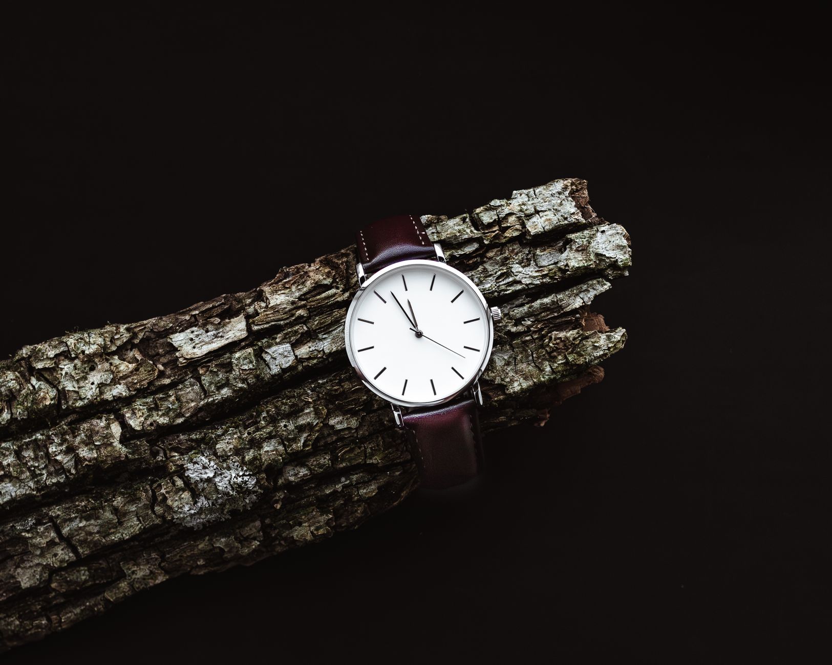 Elegant minimalist watch with a leather strap placed on rustic wood creating a bold contrast.