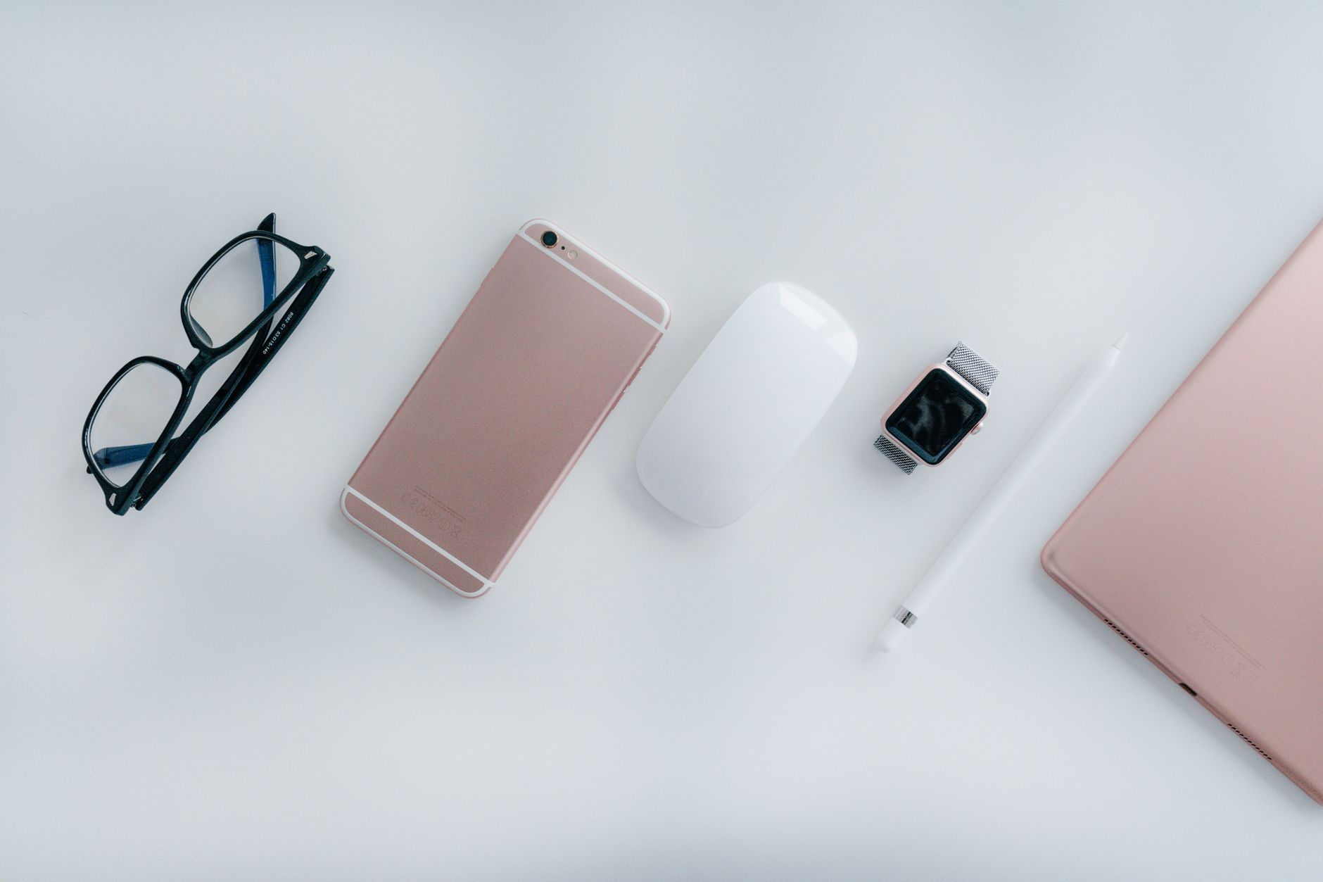 Elegant arrangement of glasses, phone, watch, mouse, pencil, and tablet on a white surface.