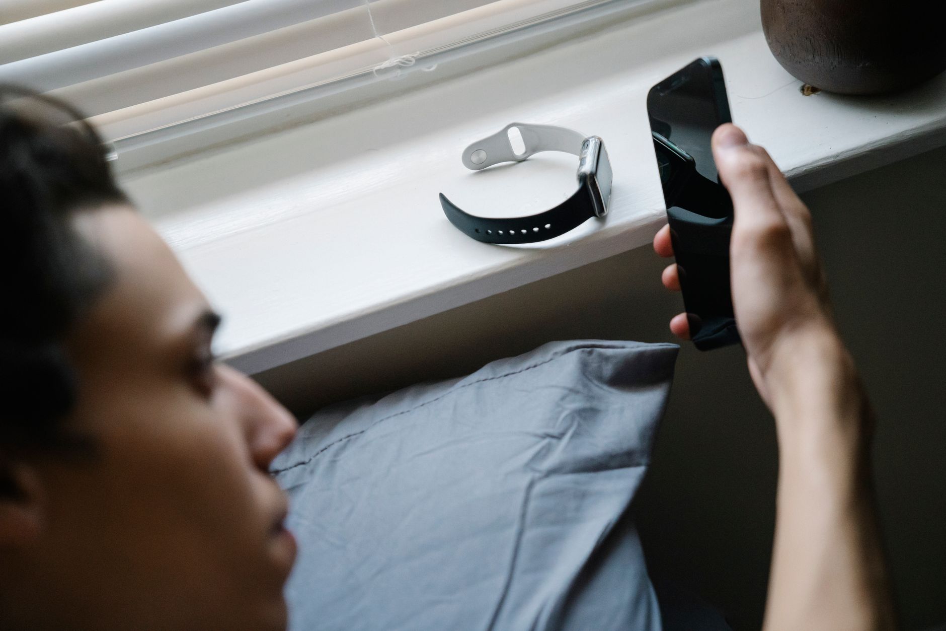 A person using a smartphone indoors with a smartwatch on a windowsill.