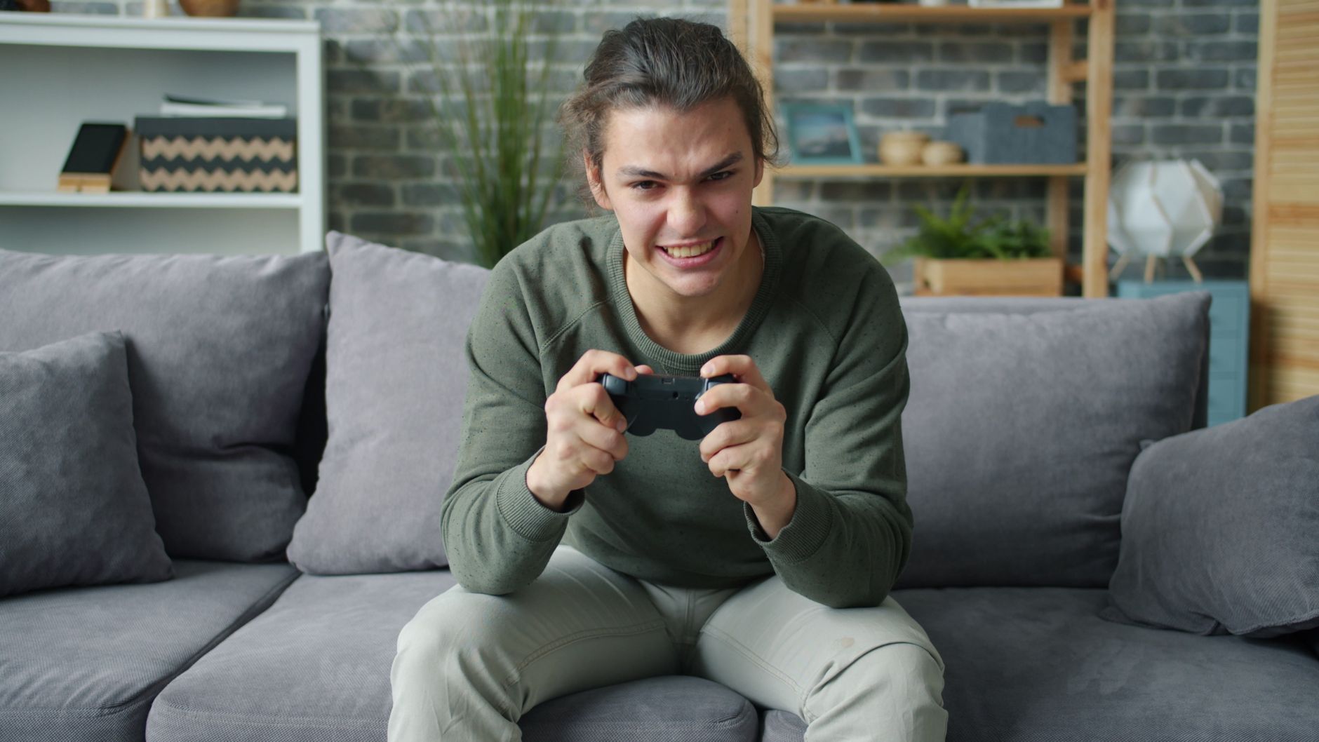 Young adult intensely playing video games on a couch in a cozy living room setting.
