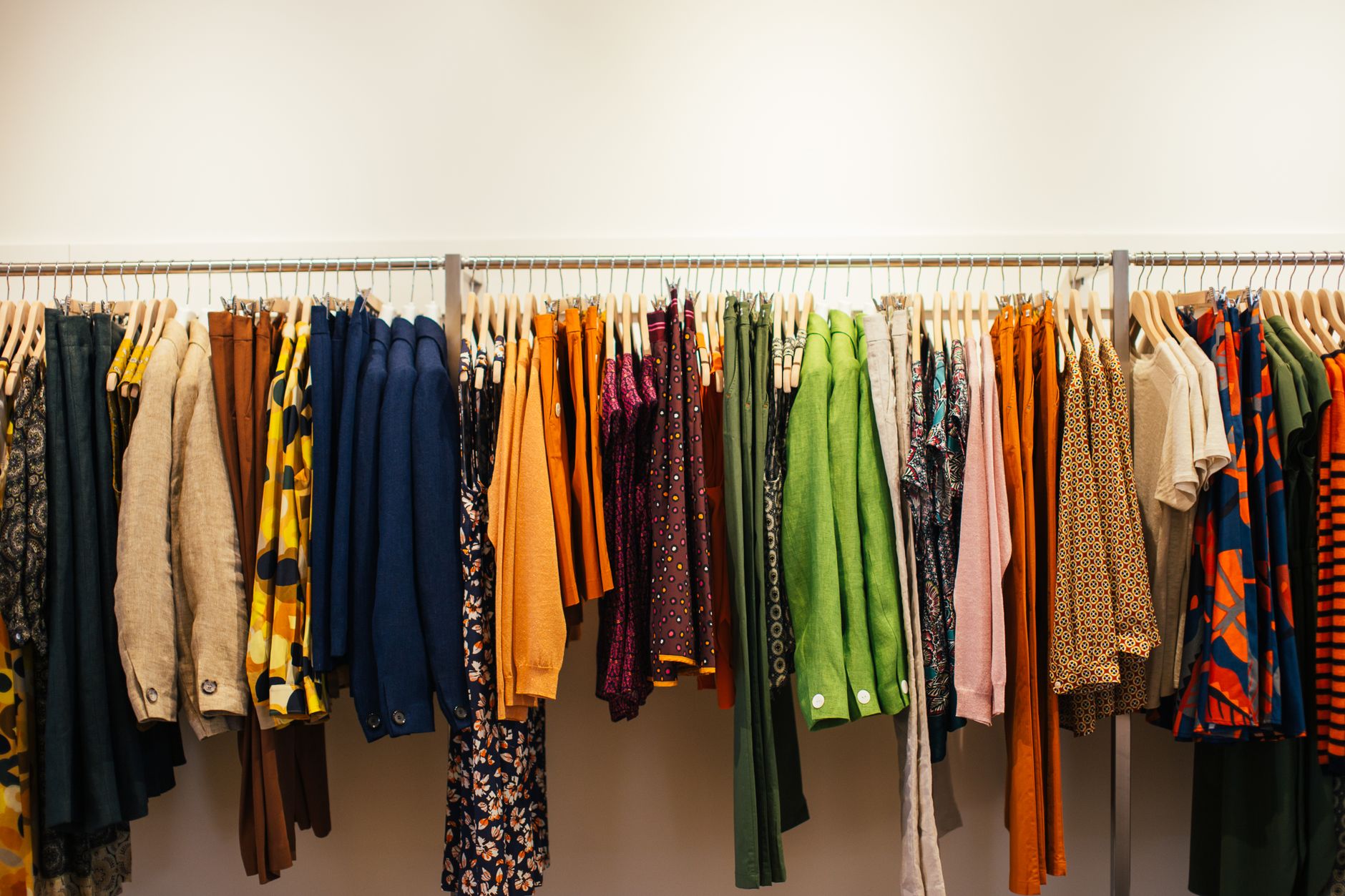 Collection of various multicolored clothes hanging on rail against light wall in shop