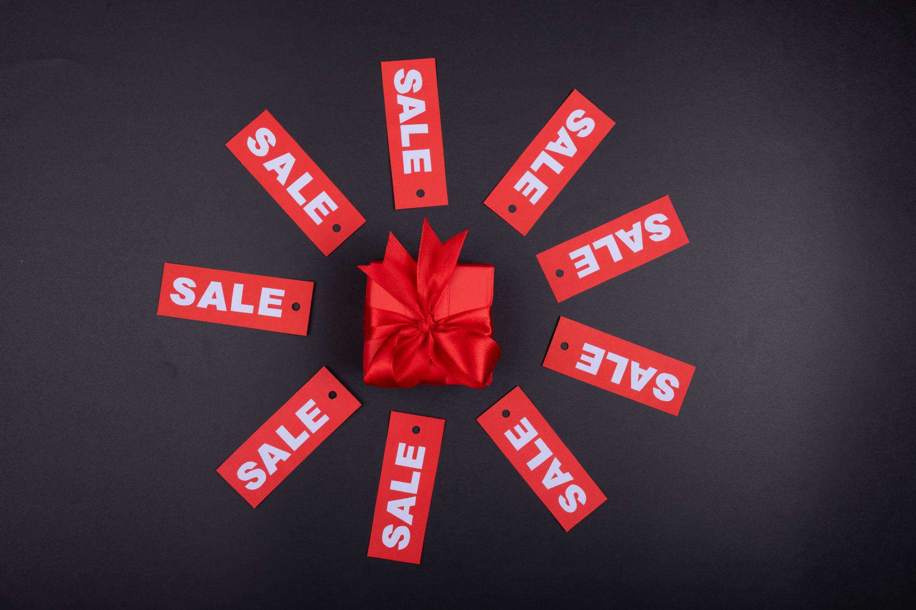 Top view of a red gift box surrounded by sale tags against a black background.