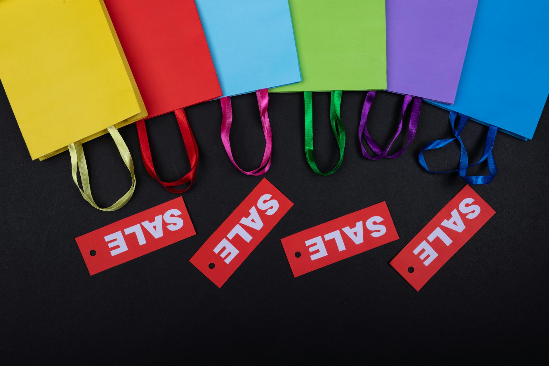 Vibrant shopping bags with sale tags on a black surface. Perfect for retail promotions.