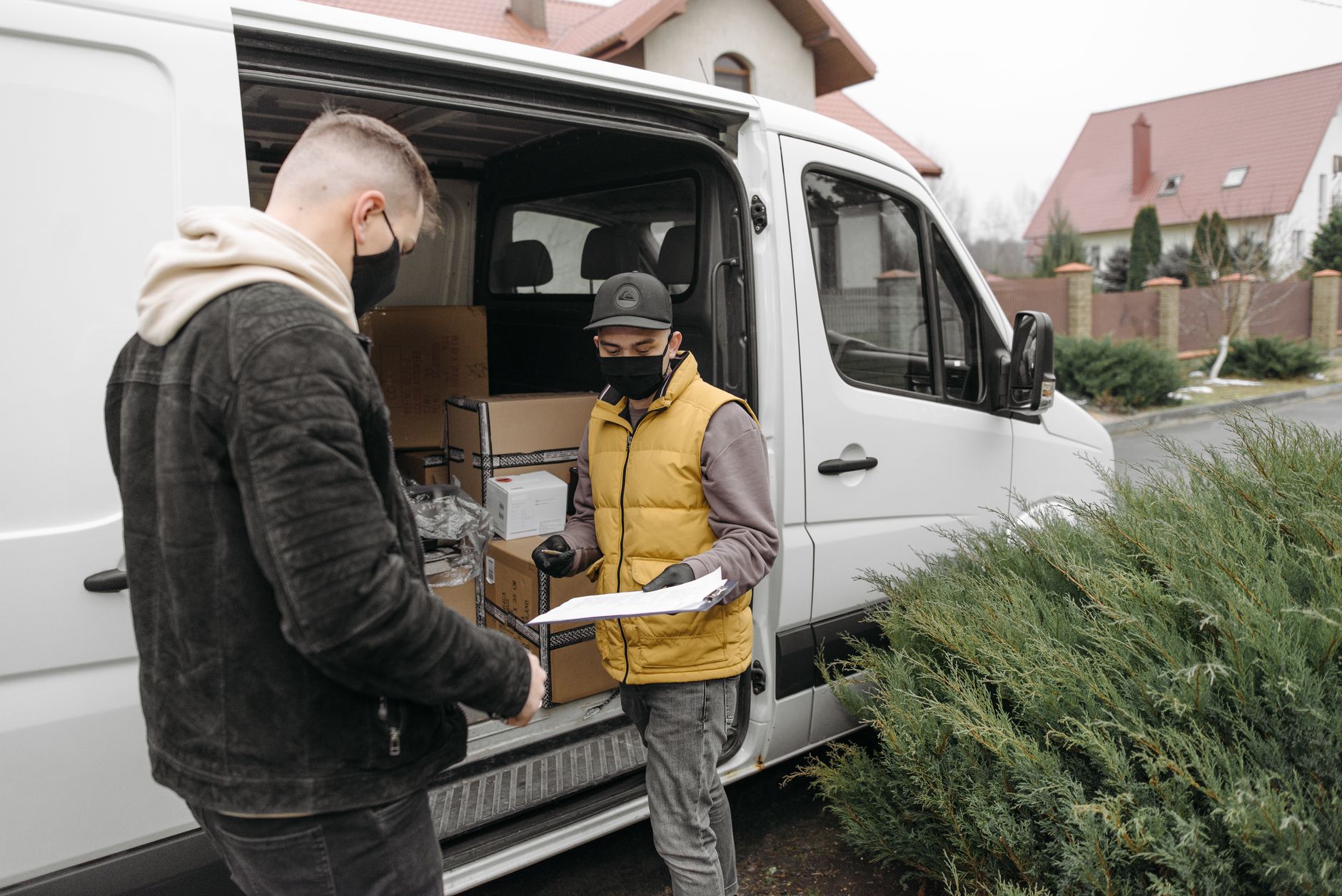 Masked deliveryman hands over parcel to customer at van during contactless delivery.