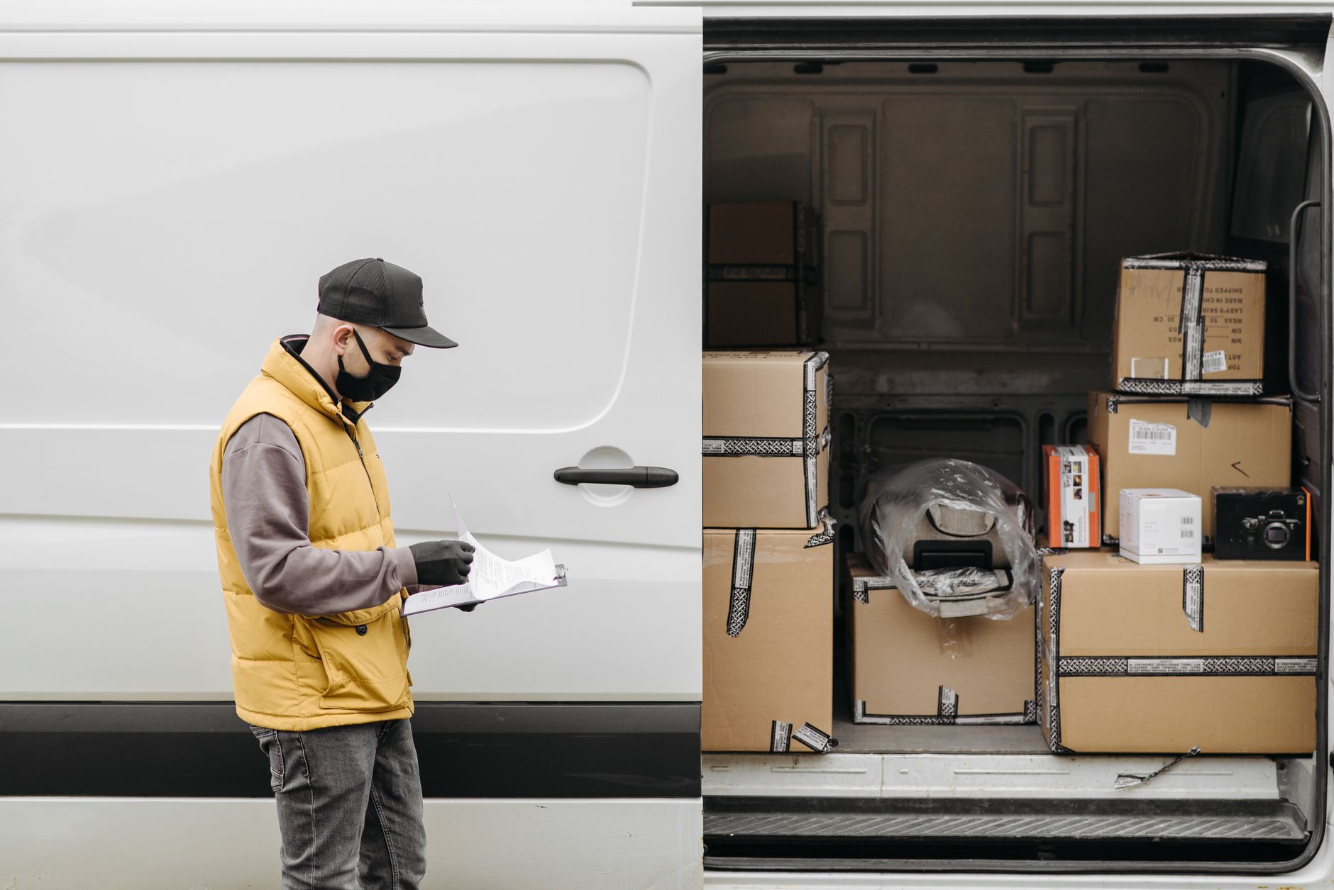 Delivery person in mask organizing cardboard packages into a van, ensuring efficient logistics.