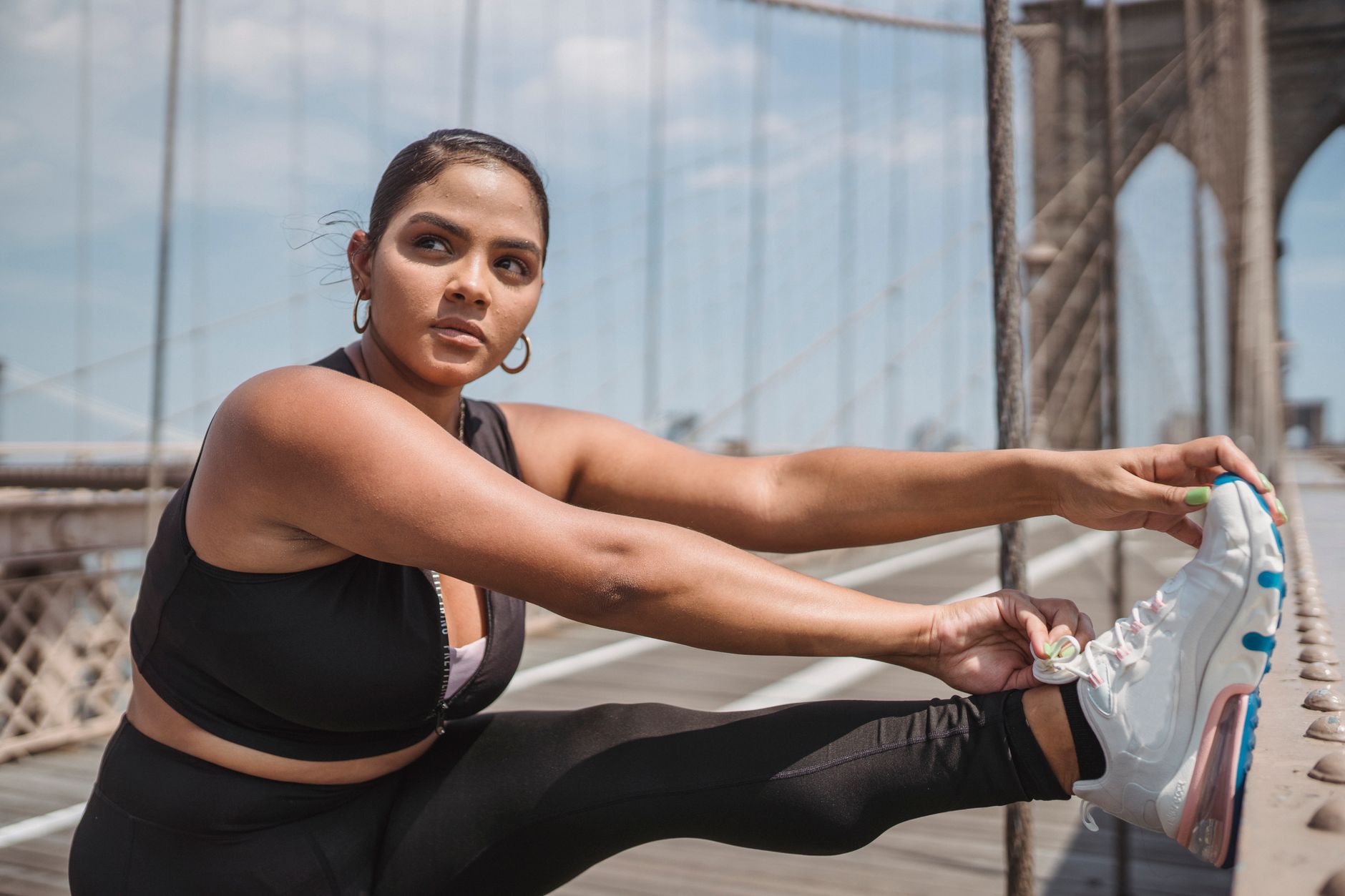Woman stretching on Brooklyn Bridge, preparing for workout in sunny weather.