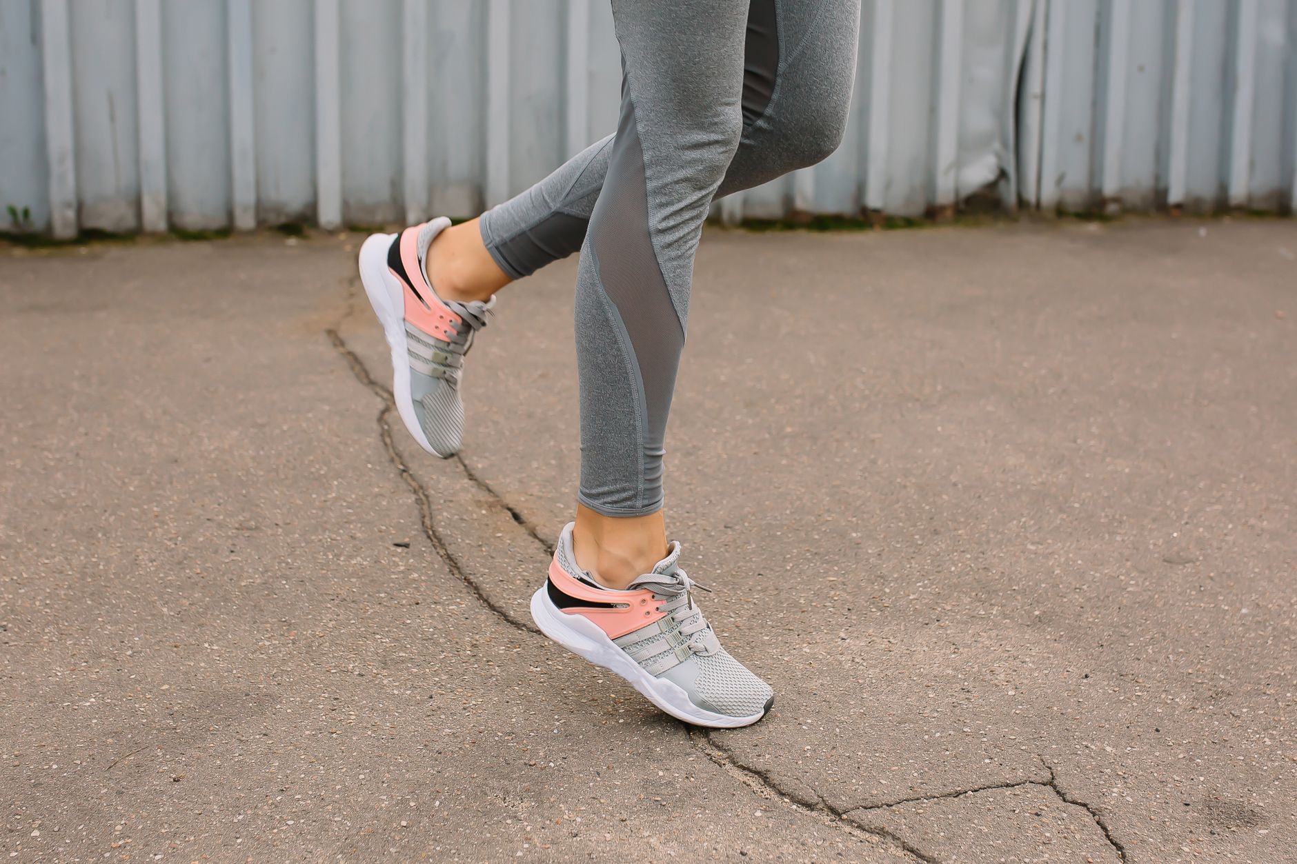 Close-up of a woman running on pavement in gray leggings and sneakers.
