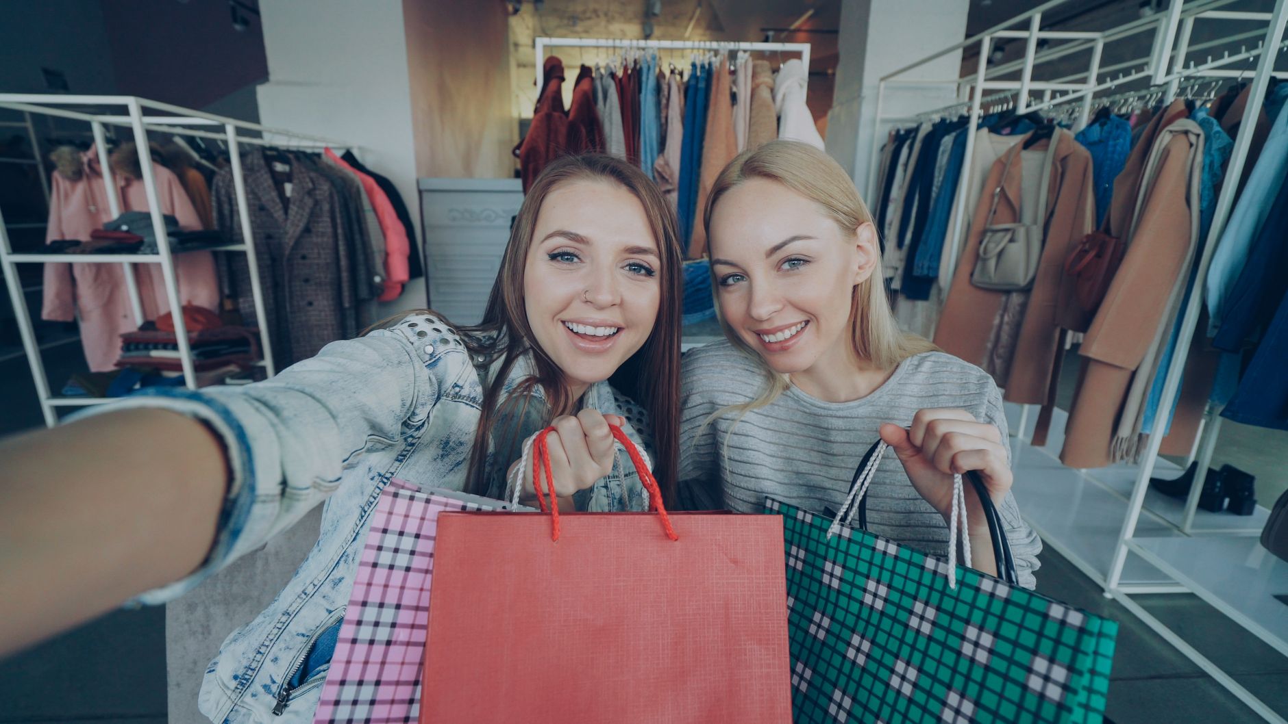 Two smiling women holding shopping bags in a stylish clothing store.
