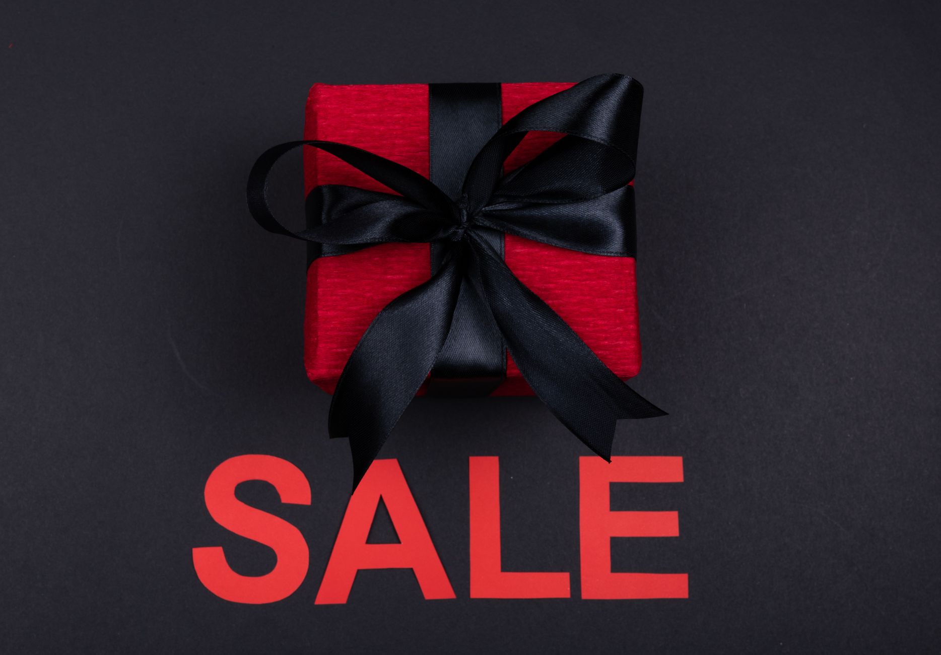 Red gift box with black ribbon and 'SALE' text on dark backdrop, perfect for marketing.