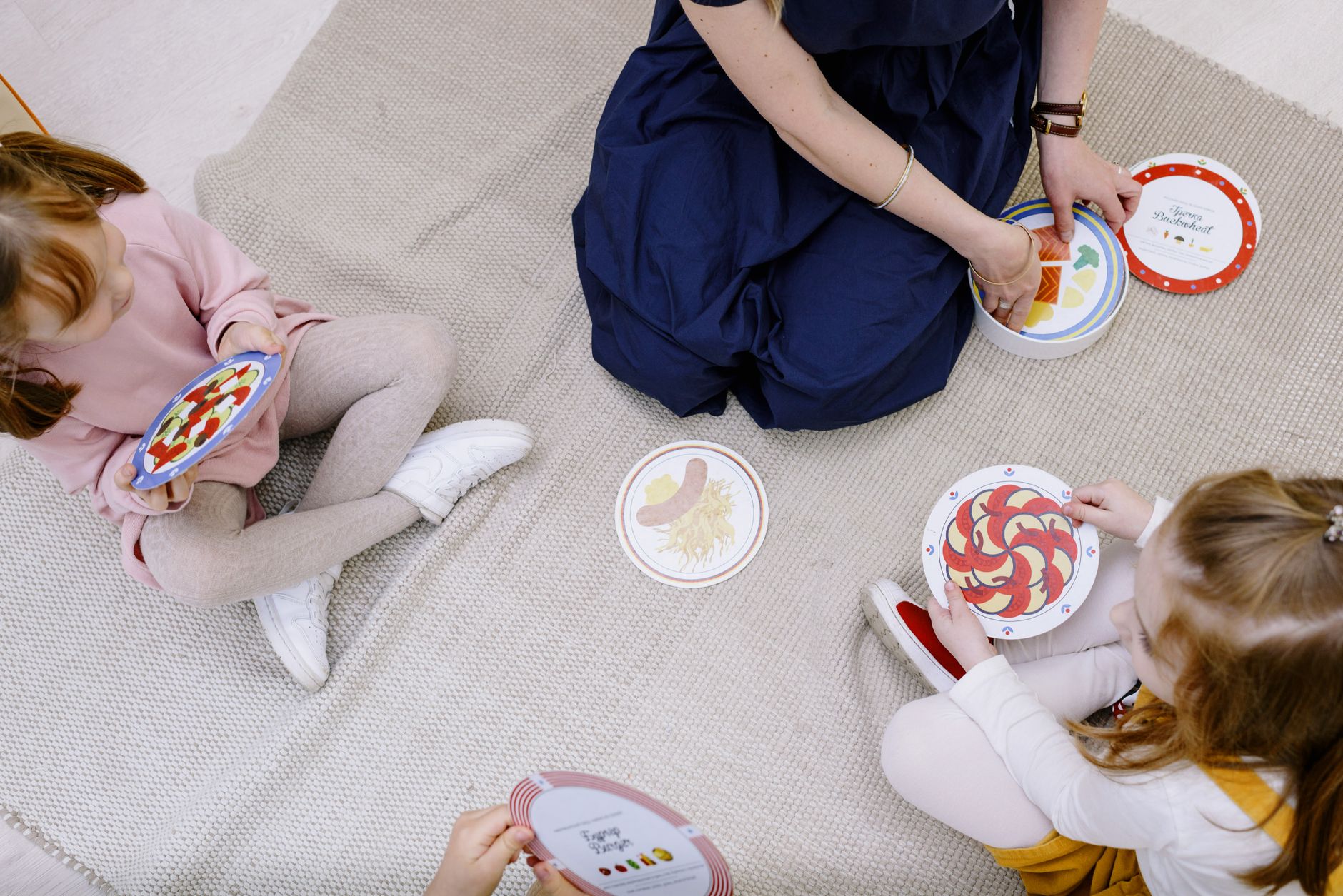 Three children and a teacher playing a card game on a blanket. Engaged and educational fun.