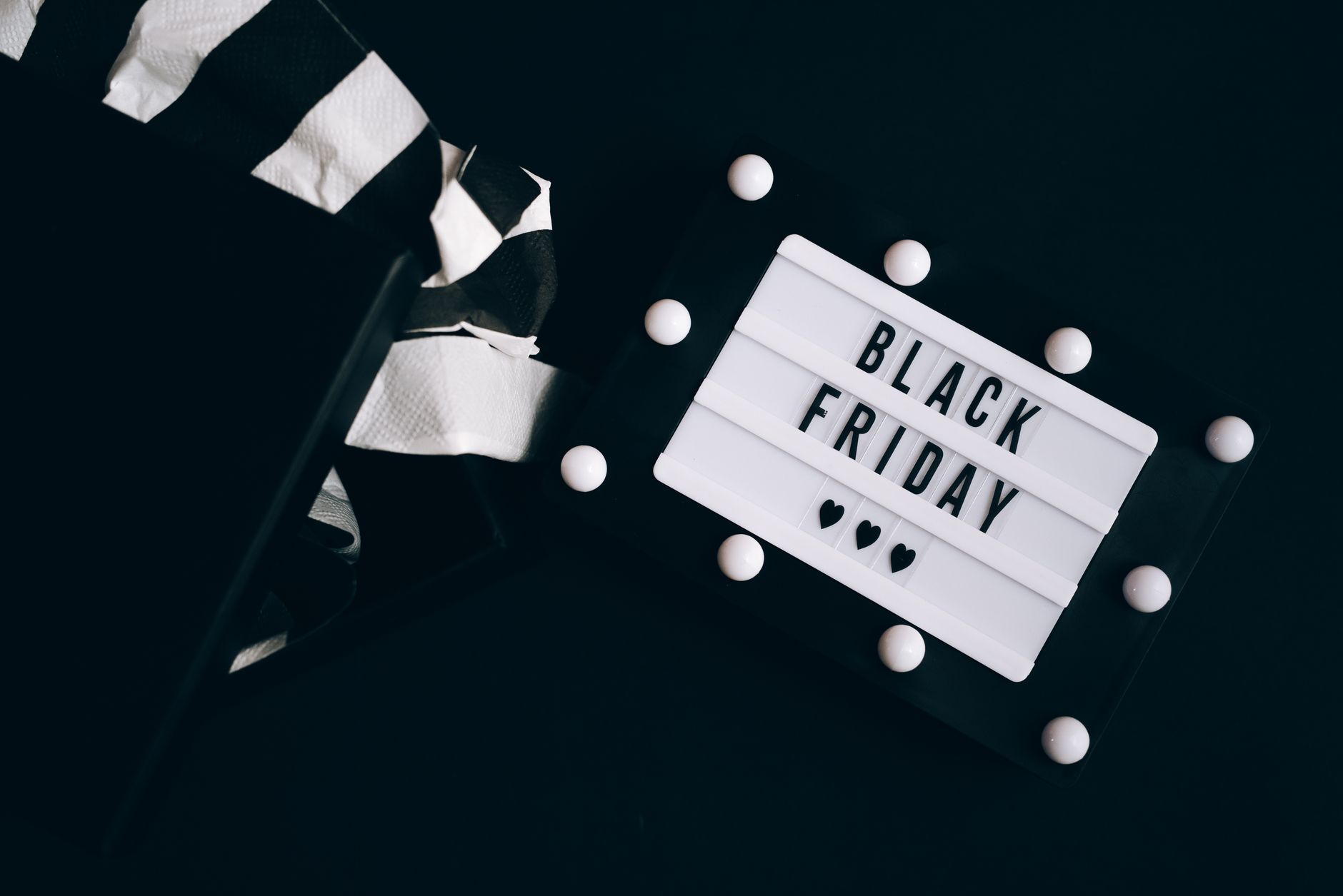 A stylish Black Friday sign next to an open gift box with striped tissue paper on a dark background.