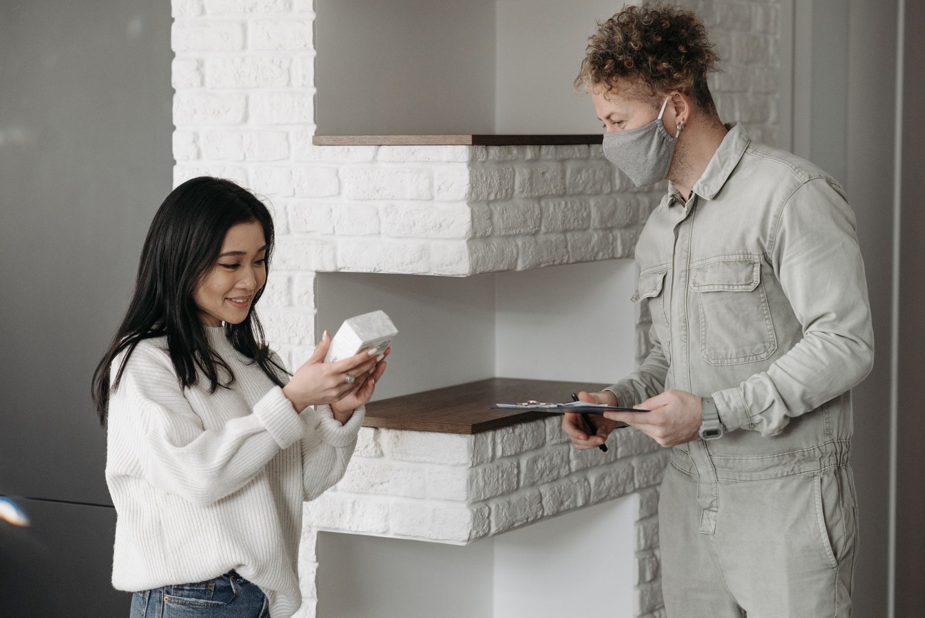 Asian woman receives a package from a courier wearing a mask indoors.