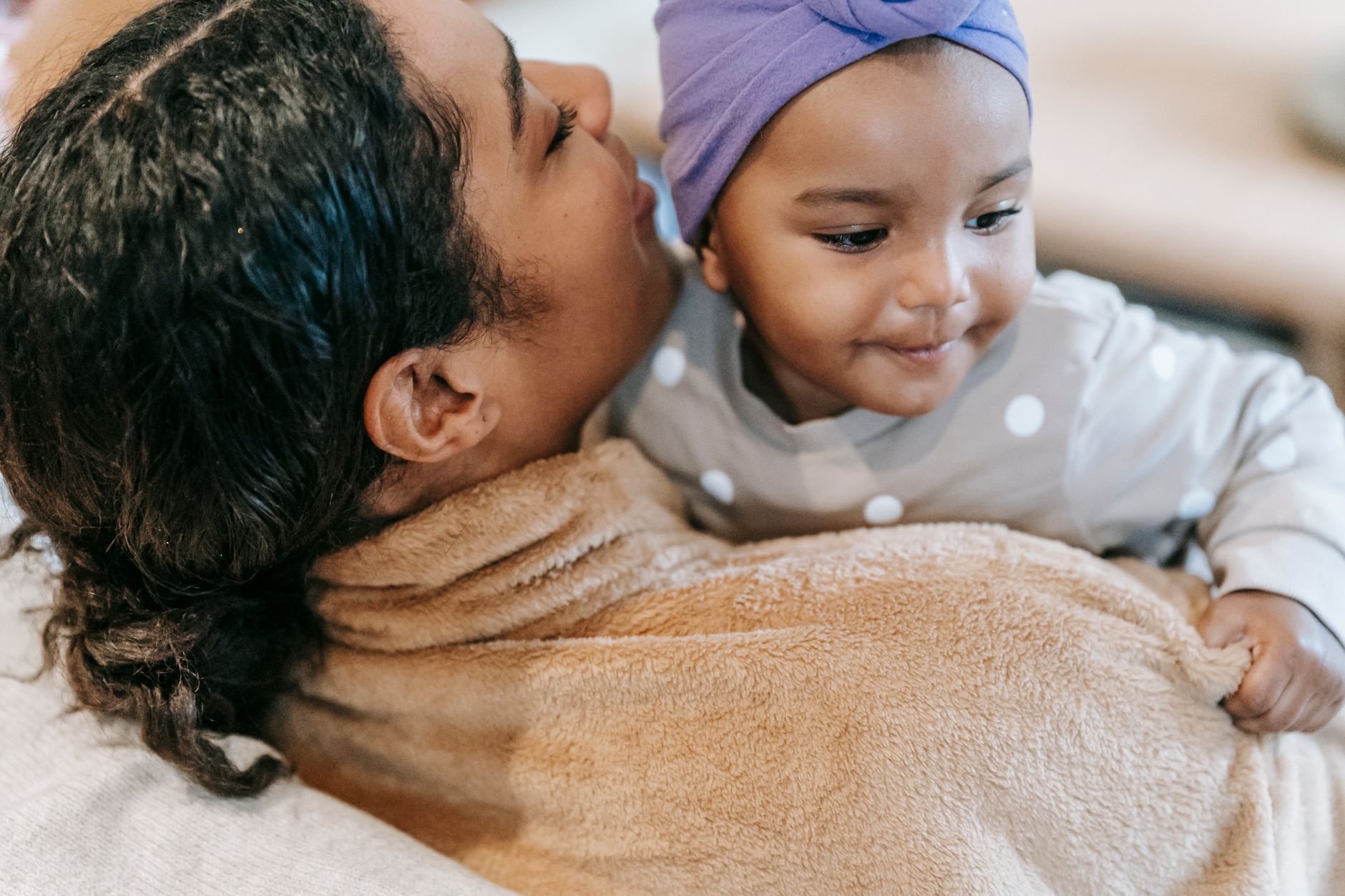 From above of crop ethnic mom speaking with cute toddler girl in headscarf on blurred background