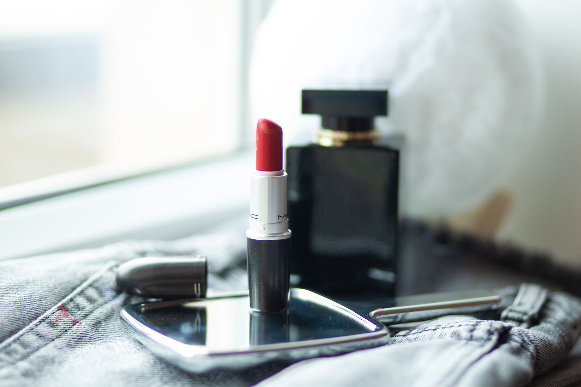 A sleek red lipstick and luxurious perfume bottle on a reflective tray, highlighting elegance and beauty.