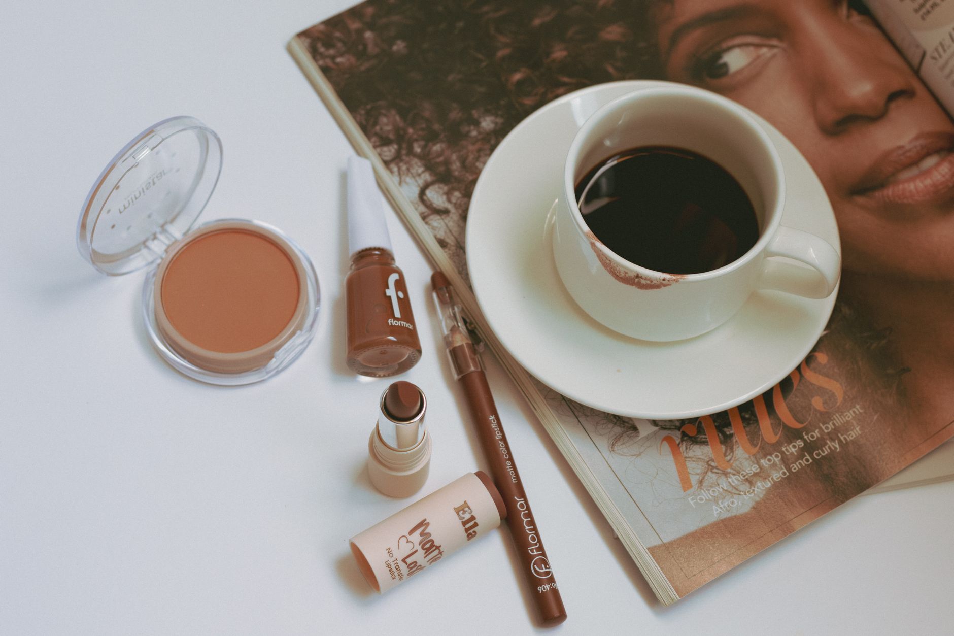 Flat lay of makeup products with coffee cup on a fashion magazine.