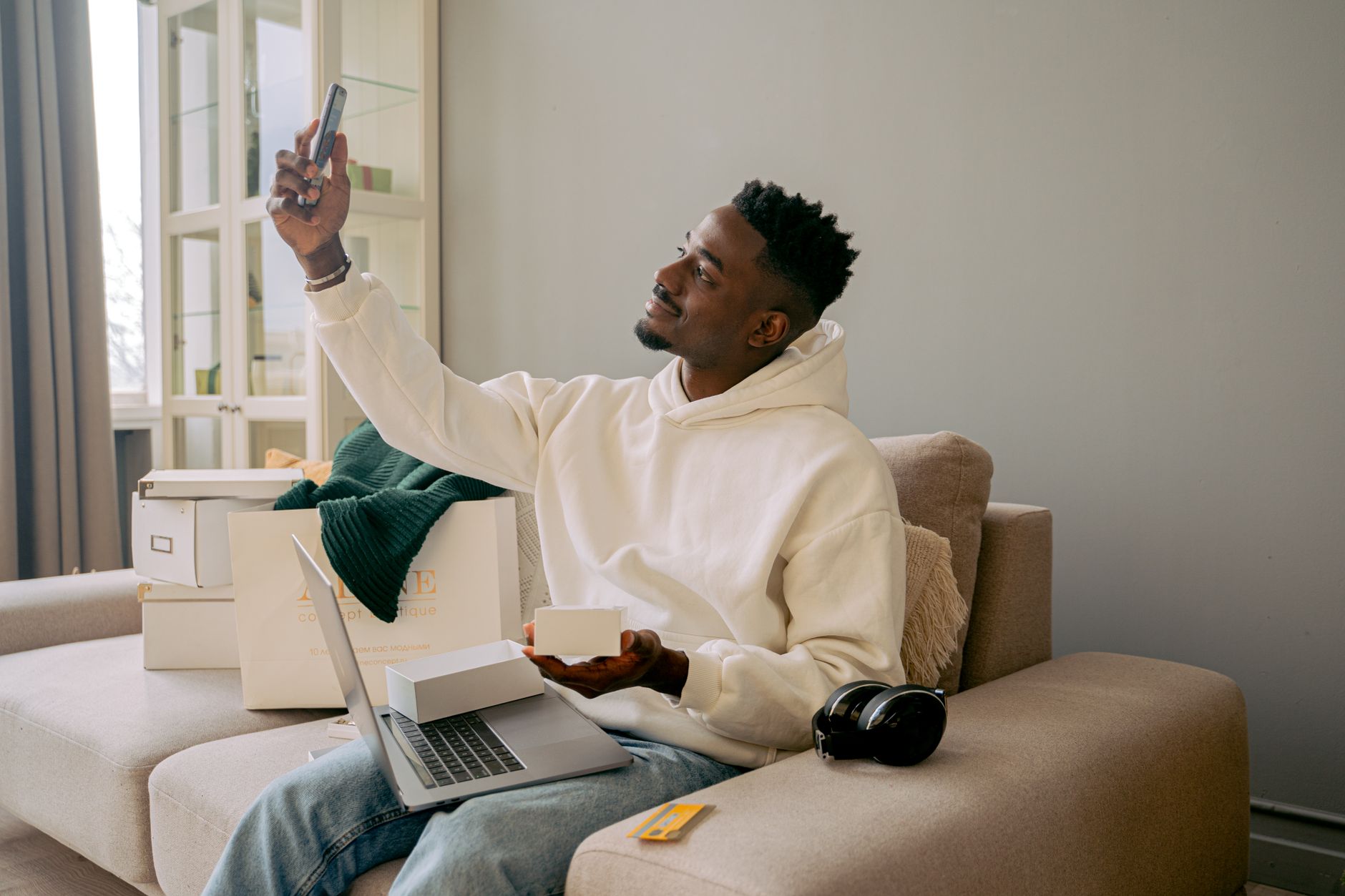 Young man taking a selfie while surrounded by online shopping boxes and a laptop.
