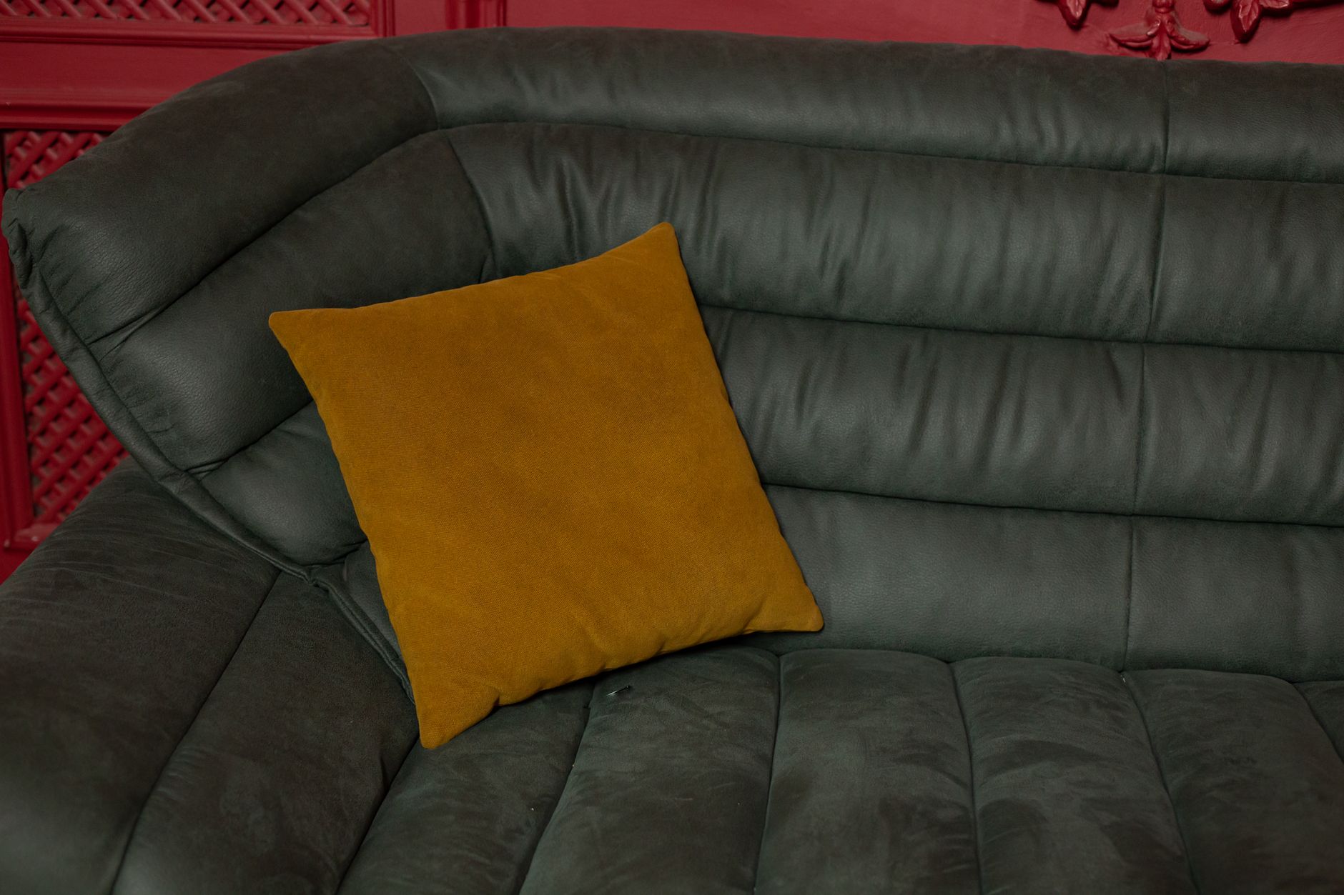 Stylish green sofa with a yellow throw pillow against a red backdrop.