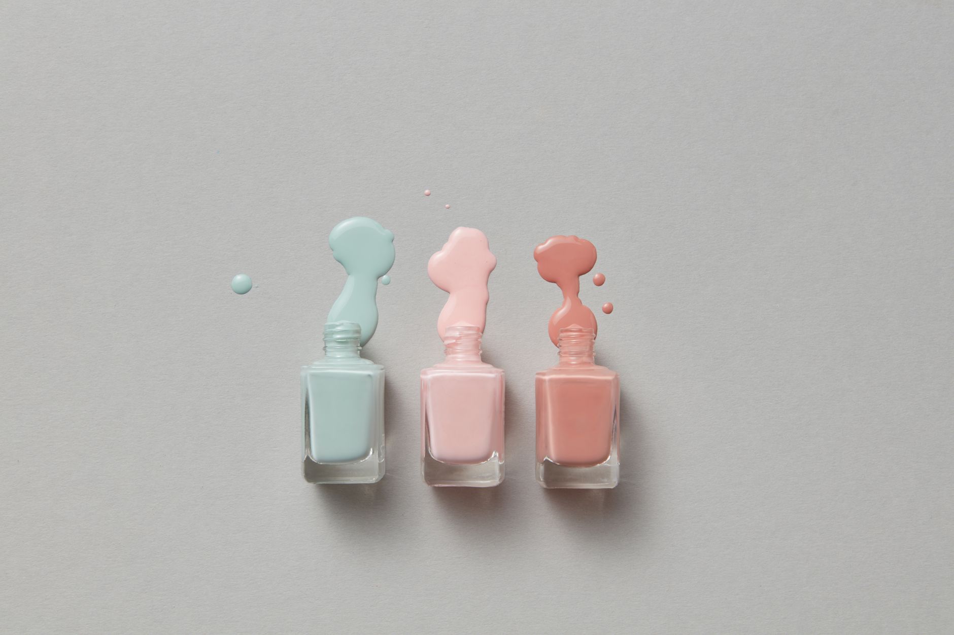 Pastel nail polish bottles with vibrant spills on a gray background.