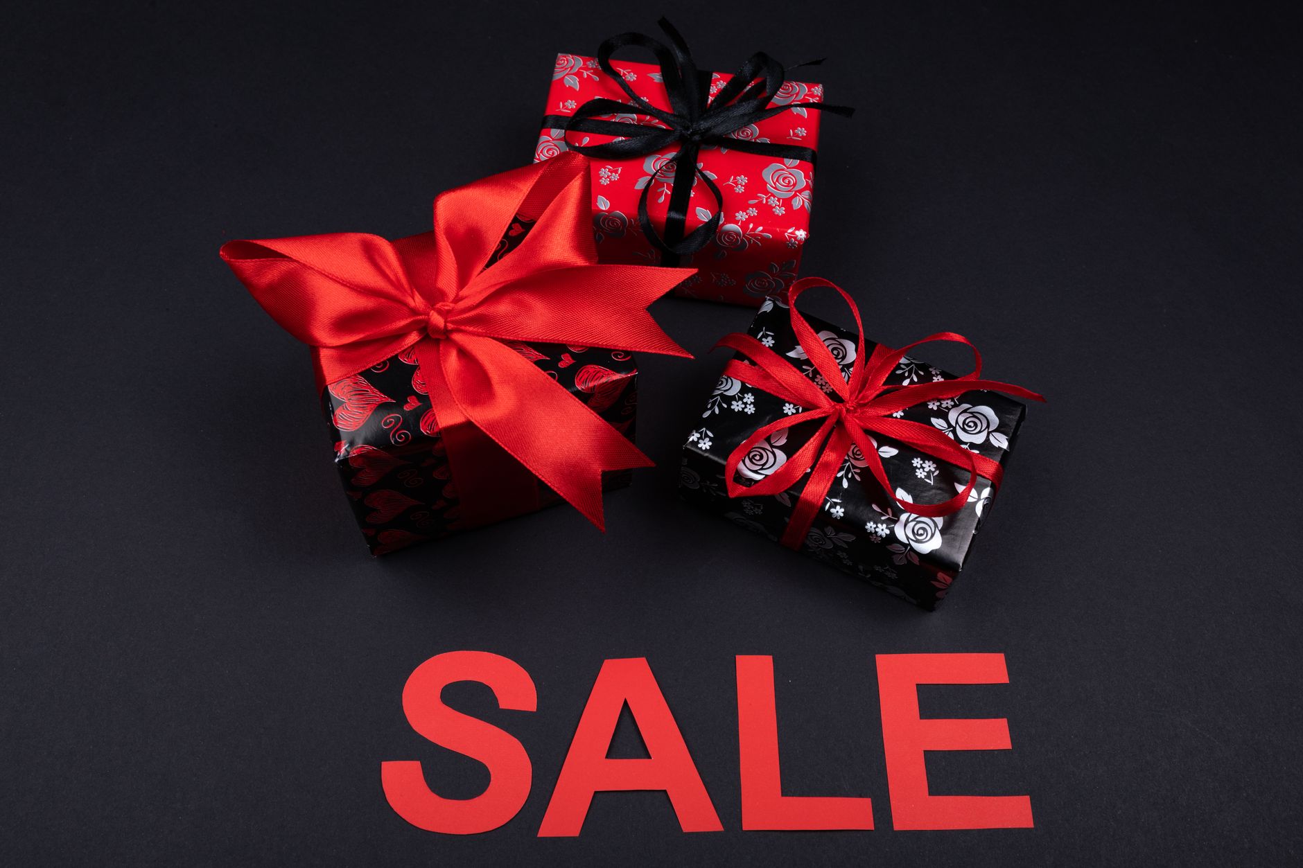Stylish red and black gift boxes with ribbons on a dark background with a sale sign.