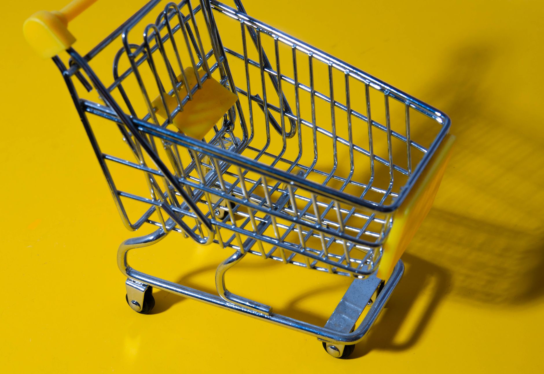 A close-up shot of a toy shopping cart on a bright yellow surface, ideal for retail or commerce themes.