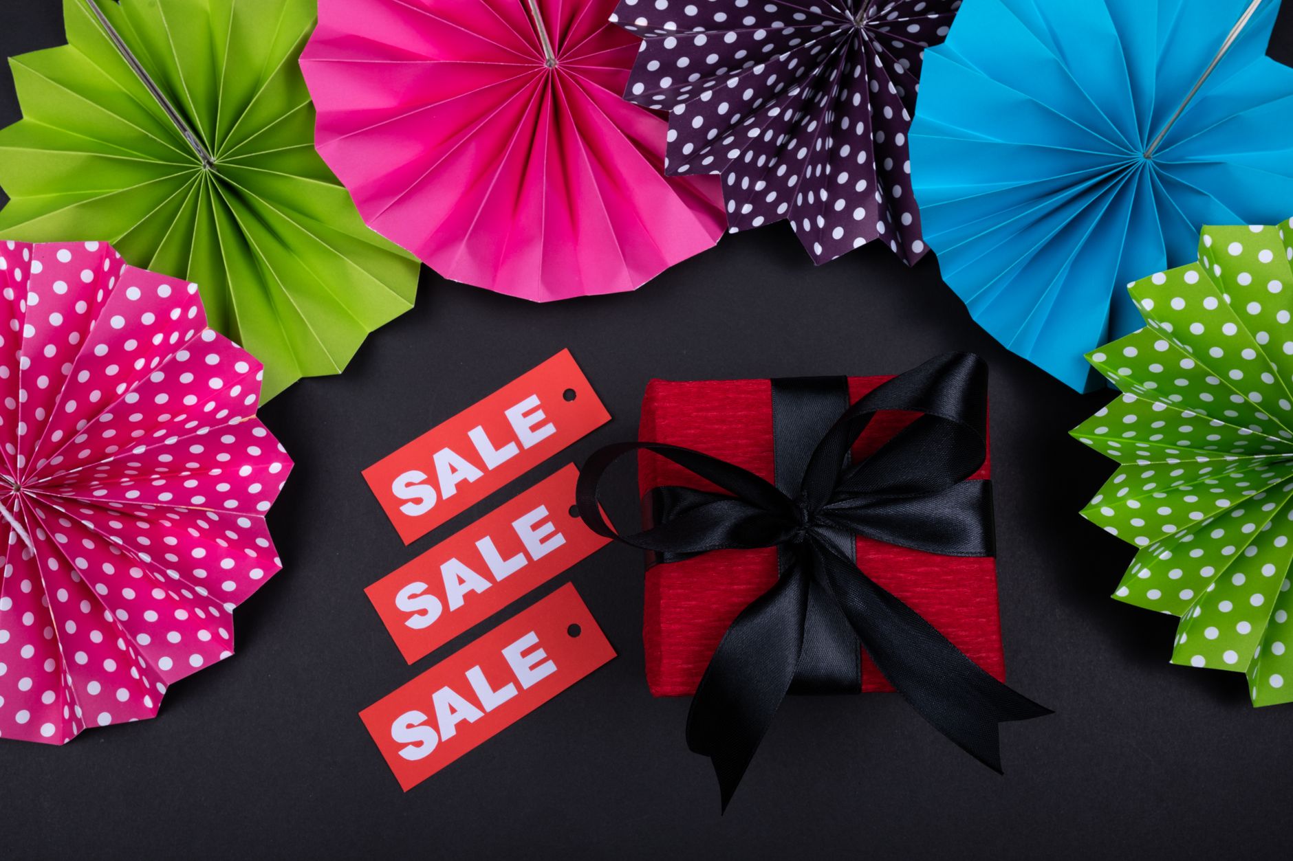 Vibrant sale display with colorful paper fans, red gift, and sale tags on black background.