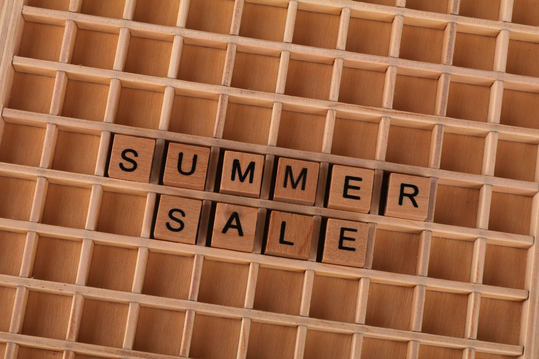 Wooden blocks arranged to spell 'Summer Sale' on a wooden grid background.