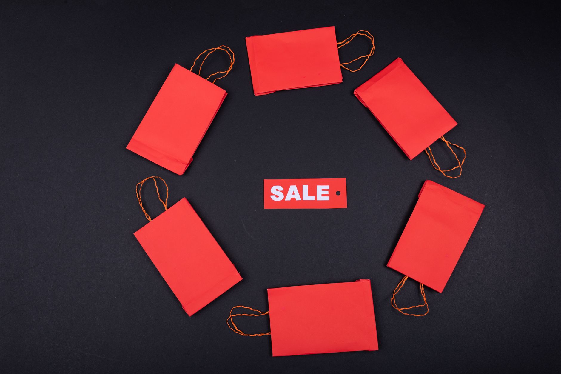 Top view of red paper bags arranged in a circle around a sale tag on a black background.
