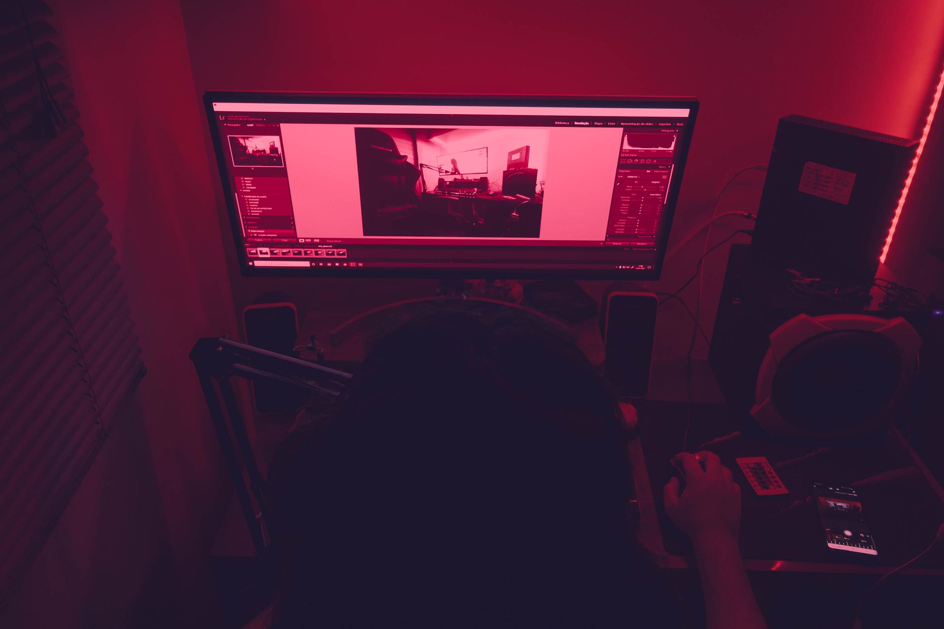 A red-illuminated desk setup with a man working on a computer at night, featuring technology elements.