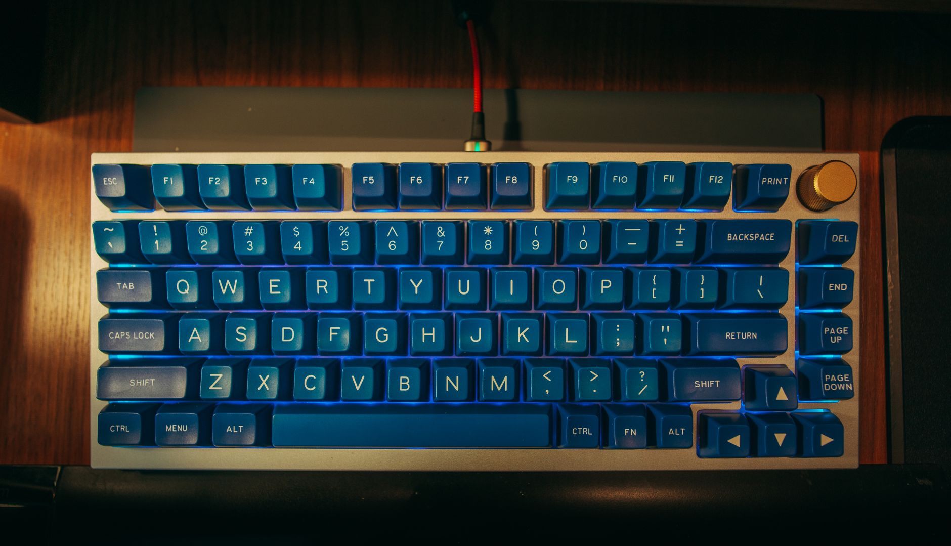 Top view of a mechanical keyboard with blue keys on a wooden desk.