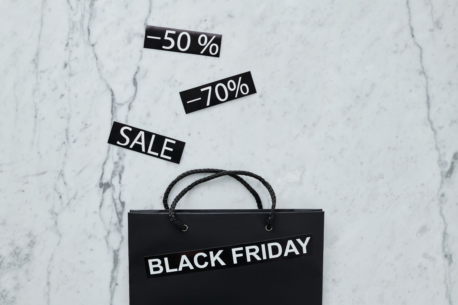 Creative flat lay of Black Friday shopping bag and sale tags on marble surface.